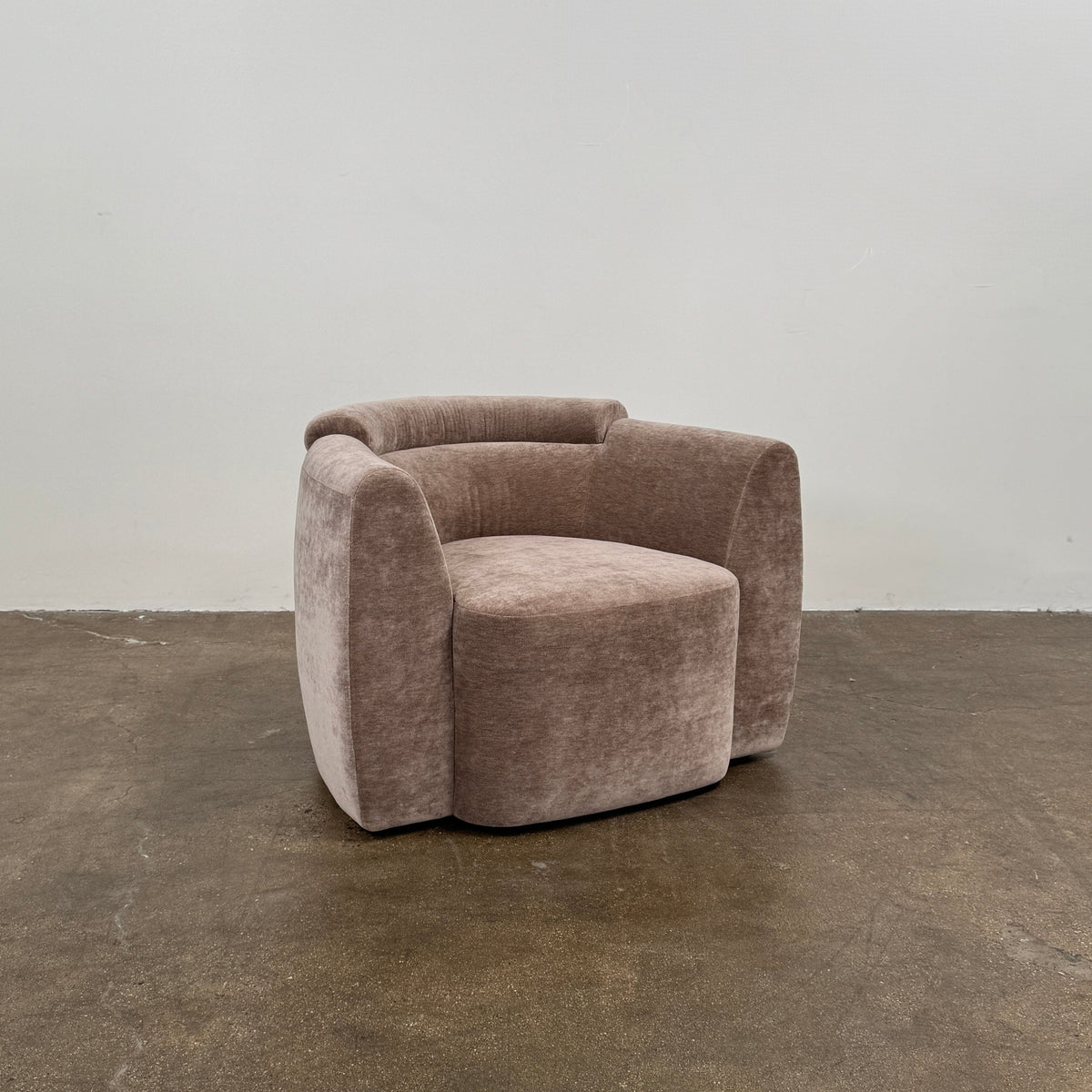 Two Daniel Boddam Wave Lounge Chairs in Maharam Mohair, featuring plush taupe upholstery with rounded backs and arms, are arranged side by side on a polished concrete floor against a plain white wall.