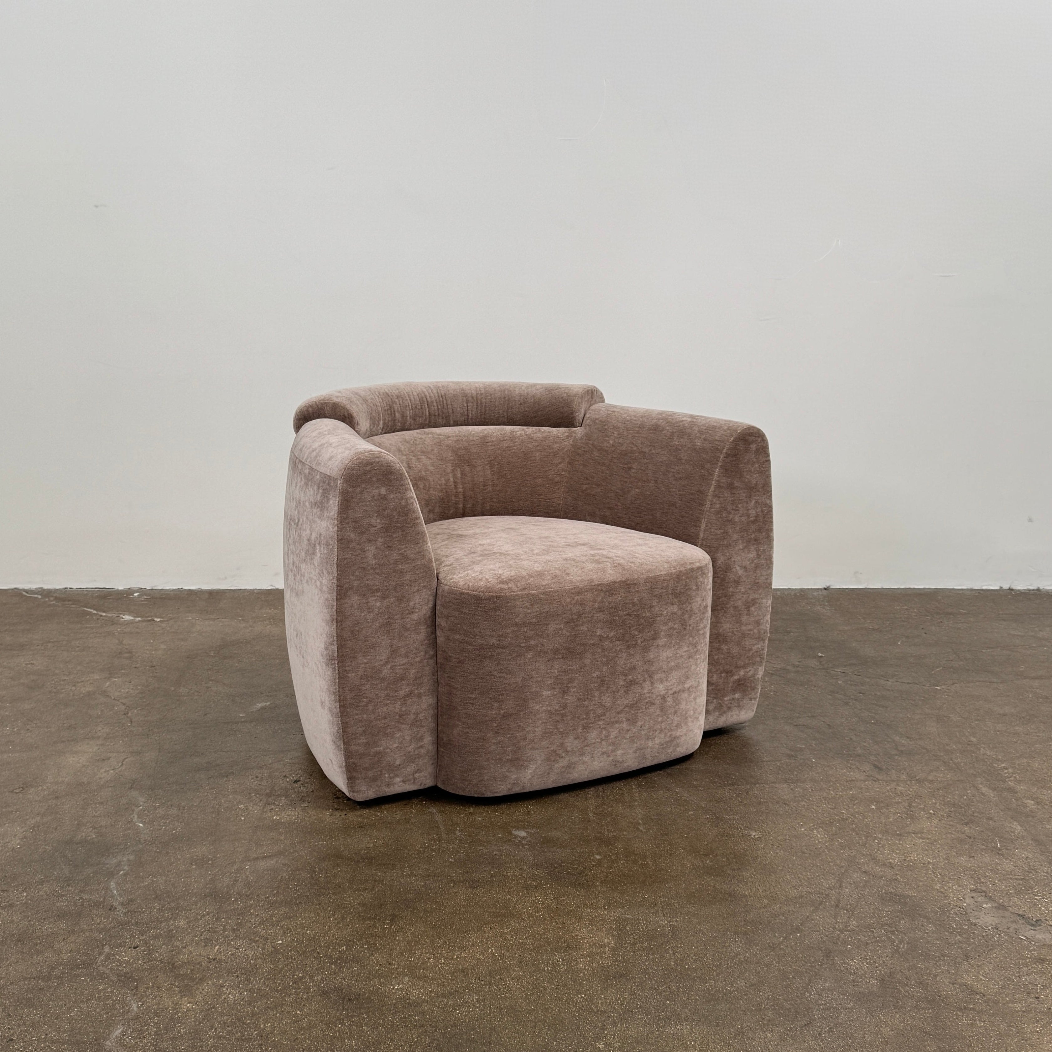 Two Daniel Boddam Wave Lounge Chairs in Maharam Mohair, featuring plush taupe upholstery with rounded backs and arms, are arranged side by side on a polished concrete floor against a plain white wall.
