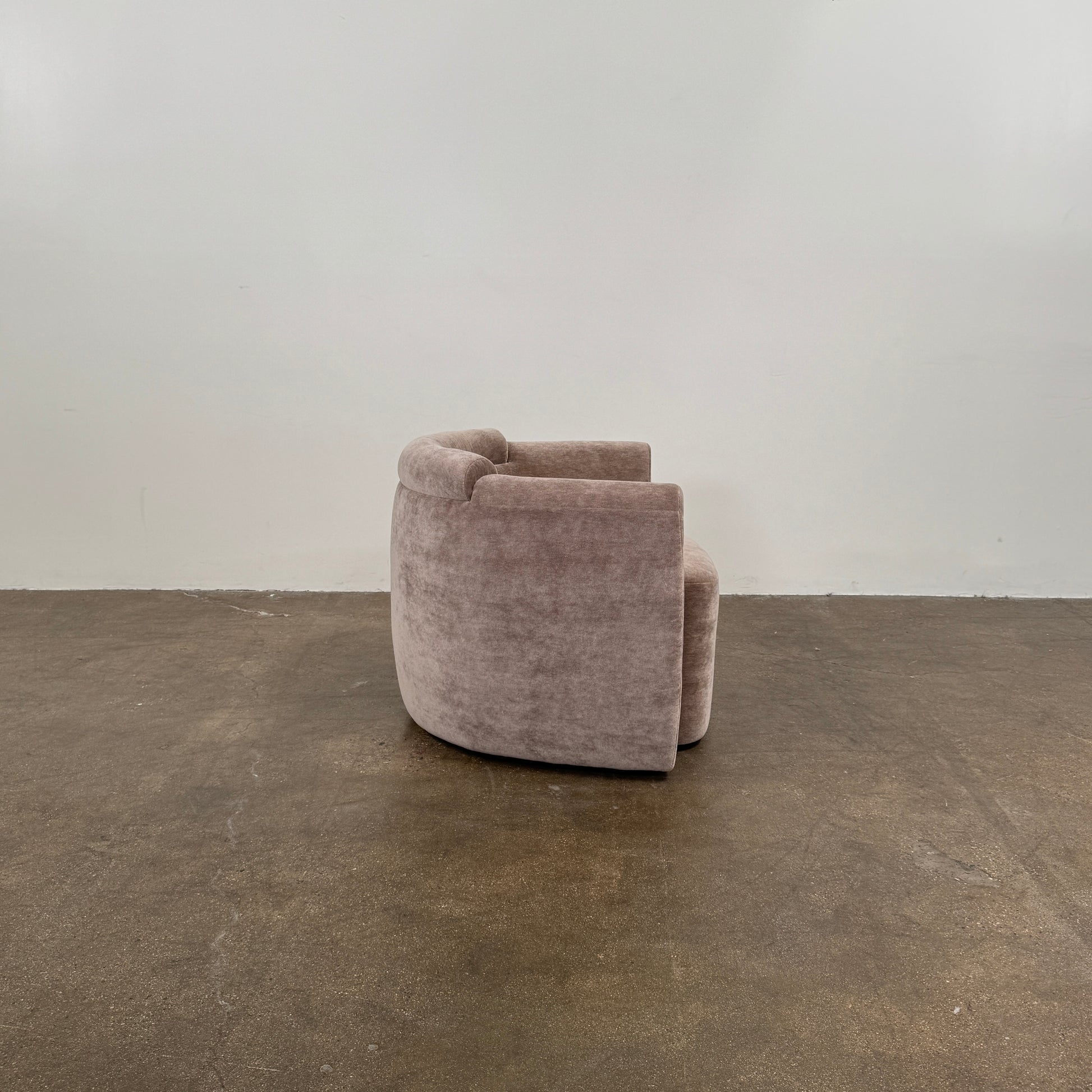Two Daniel Boddam Wave Lounge Chairs in Maharam Mohair, featuring plush taupe upholstery with rounded backs and arms, are arranged side by side on a polished concrete floor against a plain white wall.