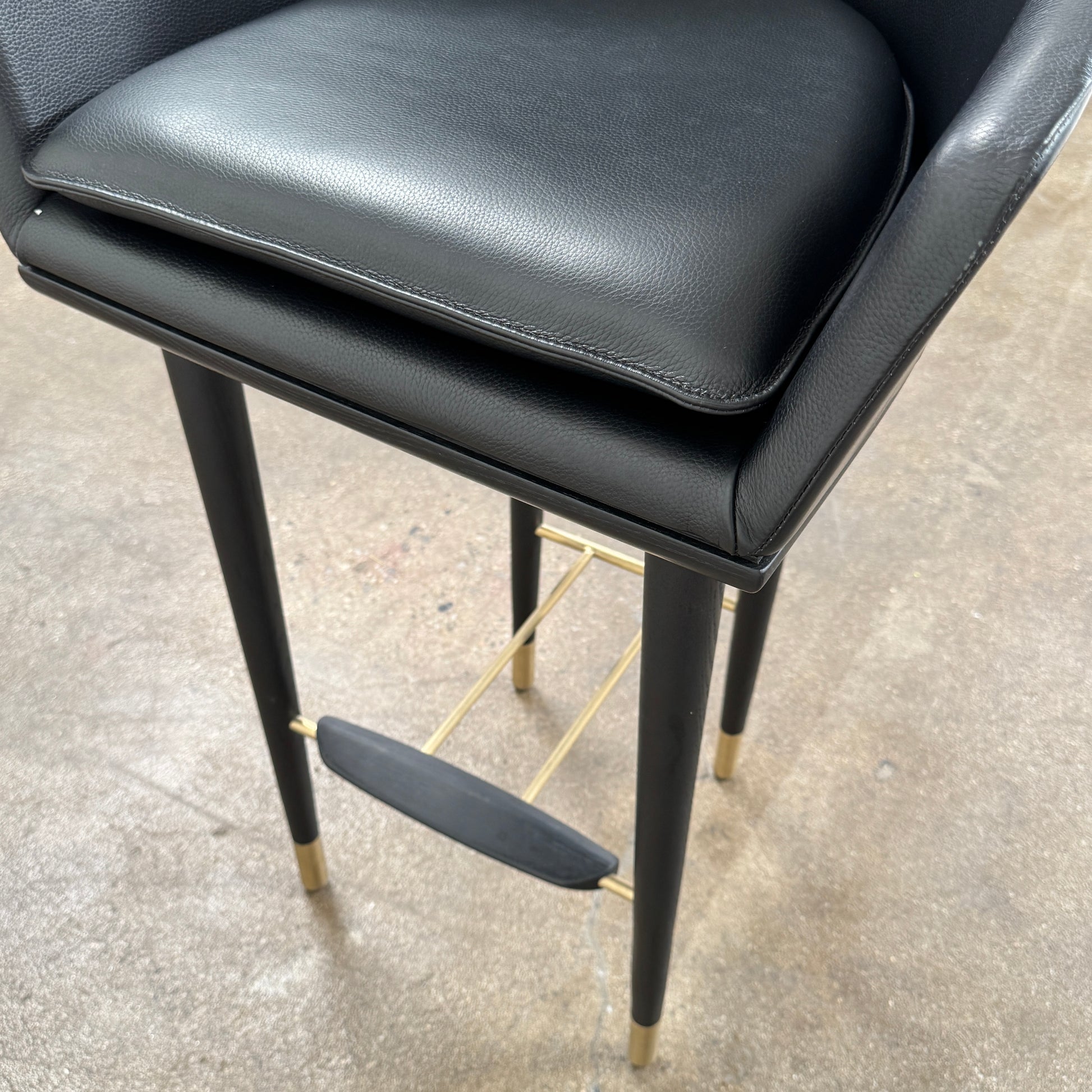 A set of three Stellar Works Lunar Bar Chairs by Steller Works, featuring black leather upholstery, armrests, and gold accents, is arranged in a row against a plain white background.