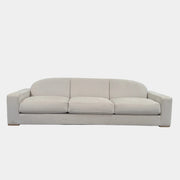The Dmitriy & Co. Erato Sofa by Dimitriy & Co is a light gray three-seater featuring low arms and wooden feet, showcased against a plain white background—an elegant example of bespoke furnishings and couture upholstery.