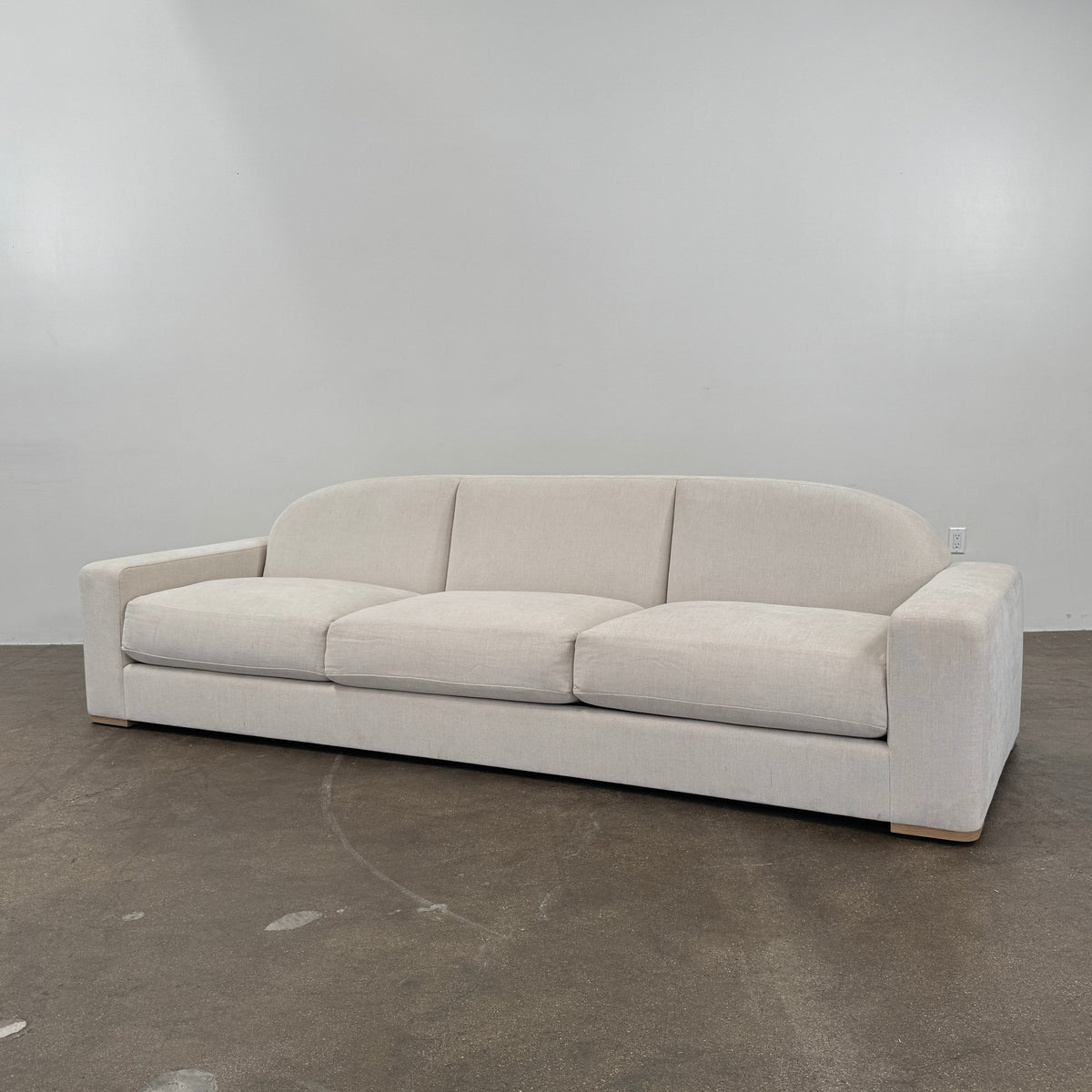 The Dmitriy & Co. Erato Sofa by Dimitriy & Co is a light gray three-seater featuring low arms and wooden feet, showcased against a plain white background—an elegant example of bespoke furnishings and couture upholstery.