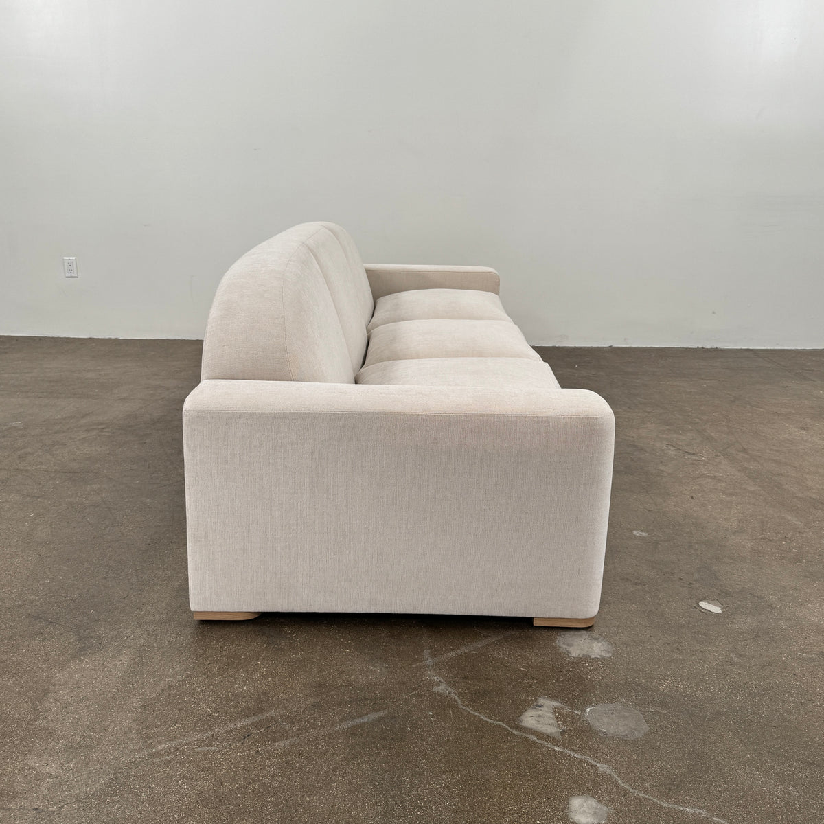 The Dmitriy & Co. Erato Sofa by Dimitriy & Co is a light gray three-seater featuring low arms and wooden feet, showcased against a plain white background—an elegant example of bespoke furnishings and couture upholstery.