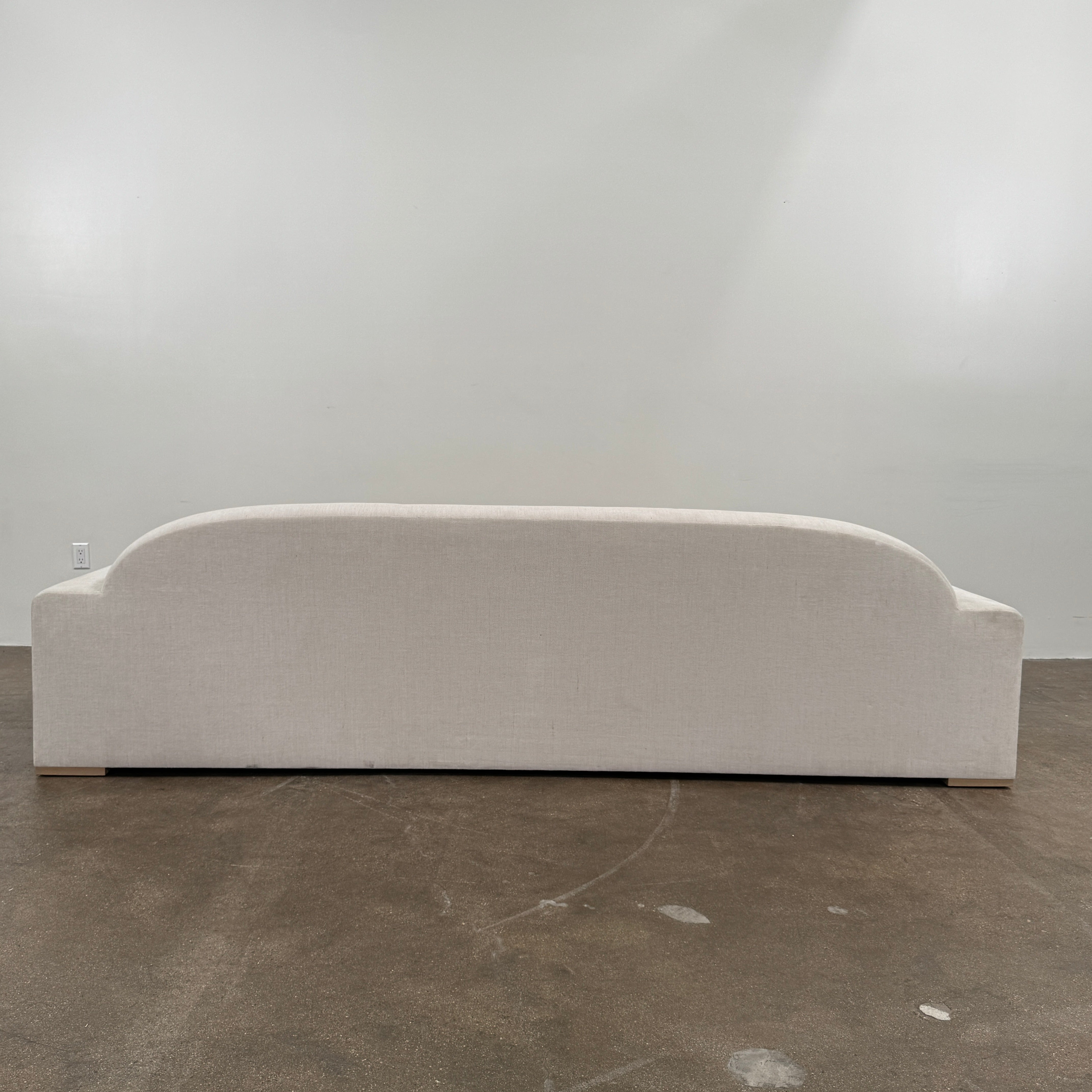 The Dmitriy & Co. Erato Sofa by Dimitriy & Co is a light gray three-seater featuring low arms and wooden feet, showcased against a plain white background—an elegant example of bespoke furnishings and couture upholstery.