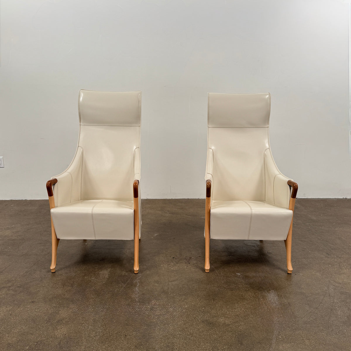 The Giorgetti “Progetti” Bergère / High-Back Lounge Chair by Giorgetti features light beige upholstery, wooden armrests and legs, and elegant ivory saddle leather accents, all inspired by the sophisticated Progetti collection, and is showcased against a plain white background.