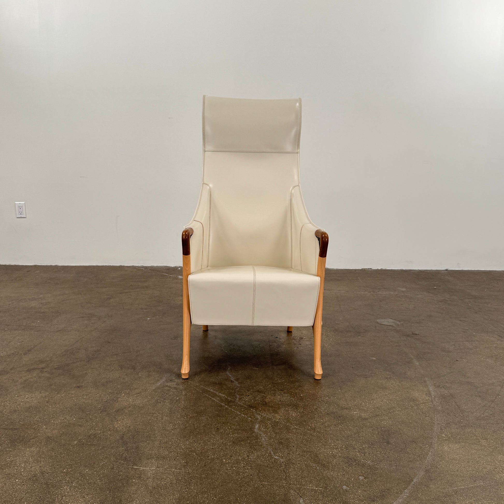 The Giorgetti “Progetti” Bergère / High-Back Lounge Chair by Giorgetti features light beige upholstery, wooden armrests and legs, and elegant ivory saddle leather accents, all inspired by the sophisticated Progetti collection, and is showcased against a plain white background.