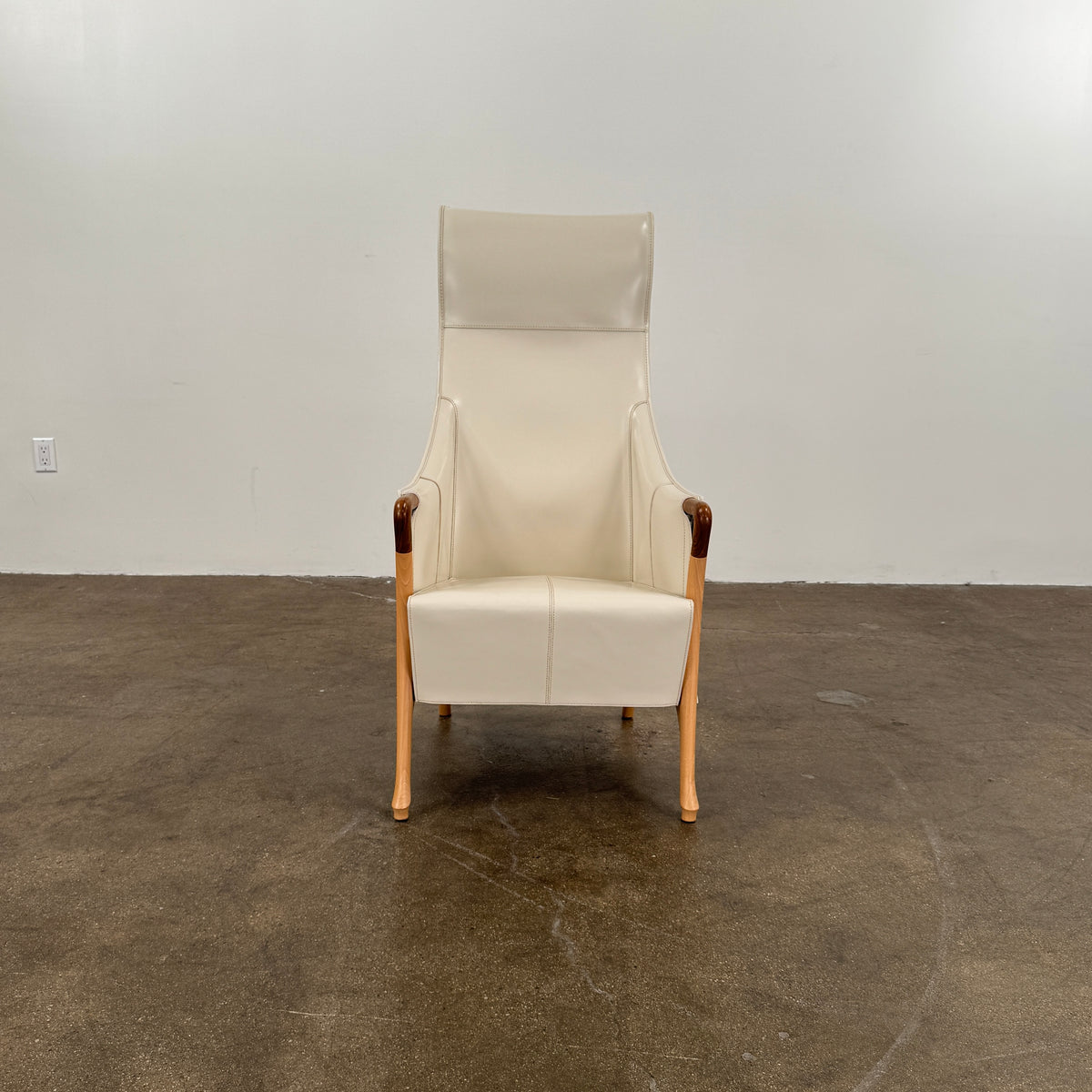 The Giorgetti “Progetti” Bergère / High-Back Lounge Chair by Giorgetti features light beige upholstery, wooden armrests and legs, and elegant ivory saddle leather accents, all inspired by the sophisticated Progetti collection, and is showcased against a plain white background.