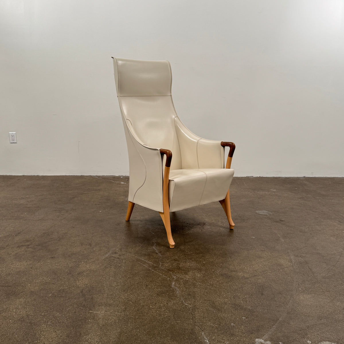 The Giorgetti “Progetti” Bergère / High-Back Lounge Chair by Giorgetti features light beige upholstery, wooden armrests and legs, and elegant ivory saddle leather accents, all inspired by the sophisticated Progetti collection, and is showcased against a plain white background.