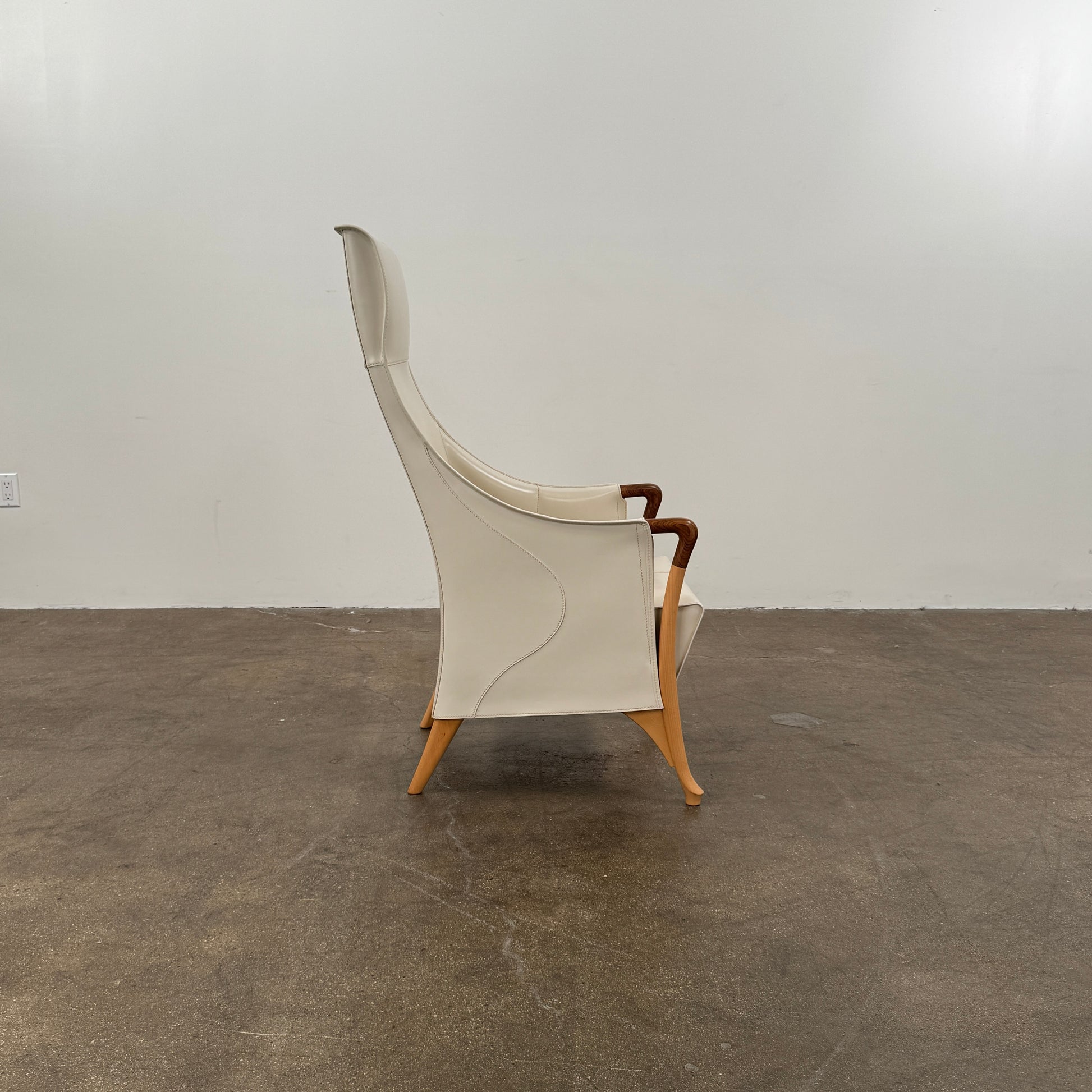 The Giorgetti “Progetti” Bergère / High-Back Lounge Chair by Giorgetti features light beige upholstery, wooden armrests and legs, and elegant ivory saddle leather accents, all inspired by the sophisticated Progetti collection, and is showcased against a plain white background.