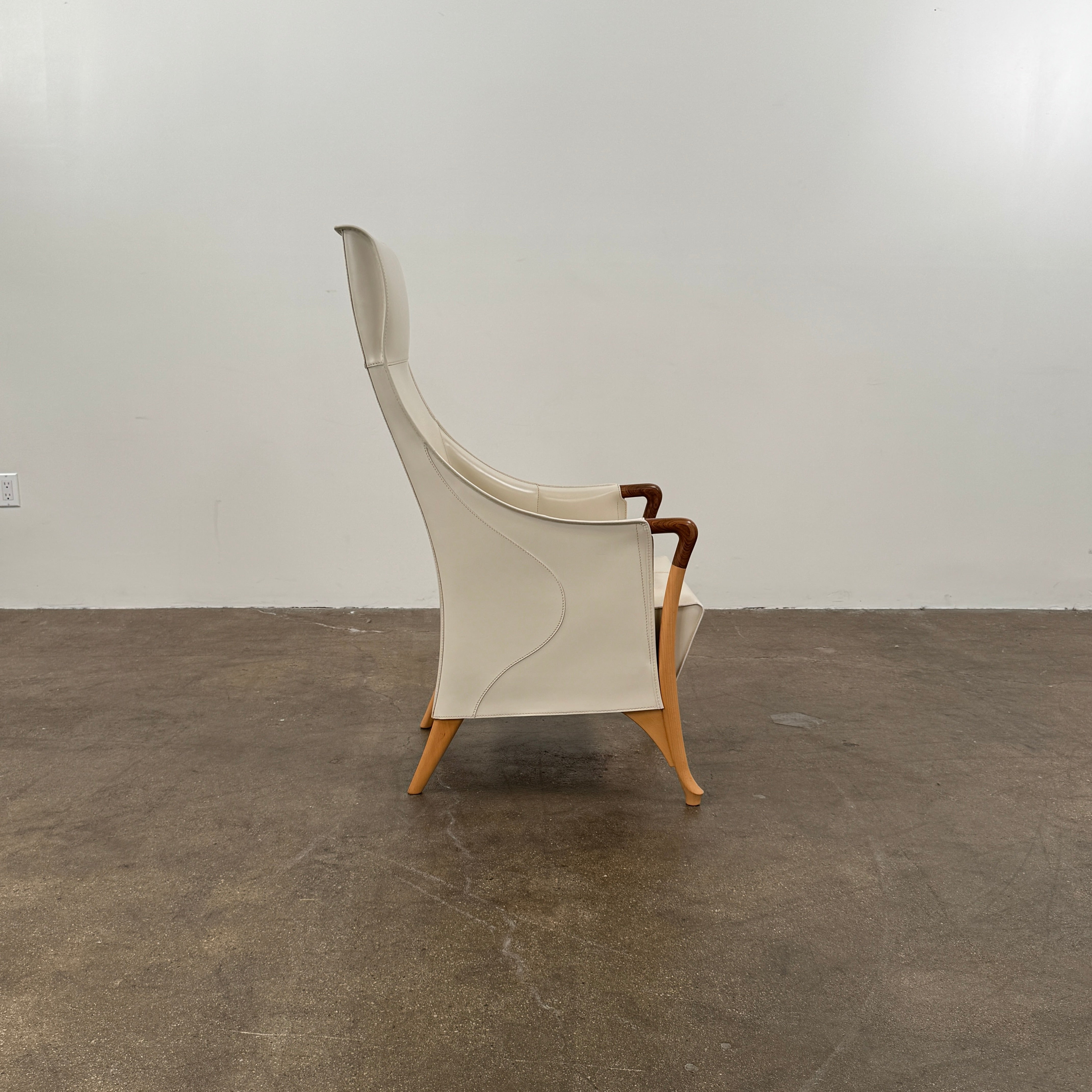 The Giorgetti “Progetti” Bergère / High-Back Lounge Chair by Giorgetti features light beige upholstery, wooden armrests and legs, and elegant ivory saddle leather accents, all inspired by the sophisticated Progetti collection, and is showcased against a plain white background.