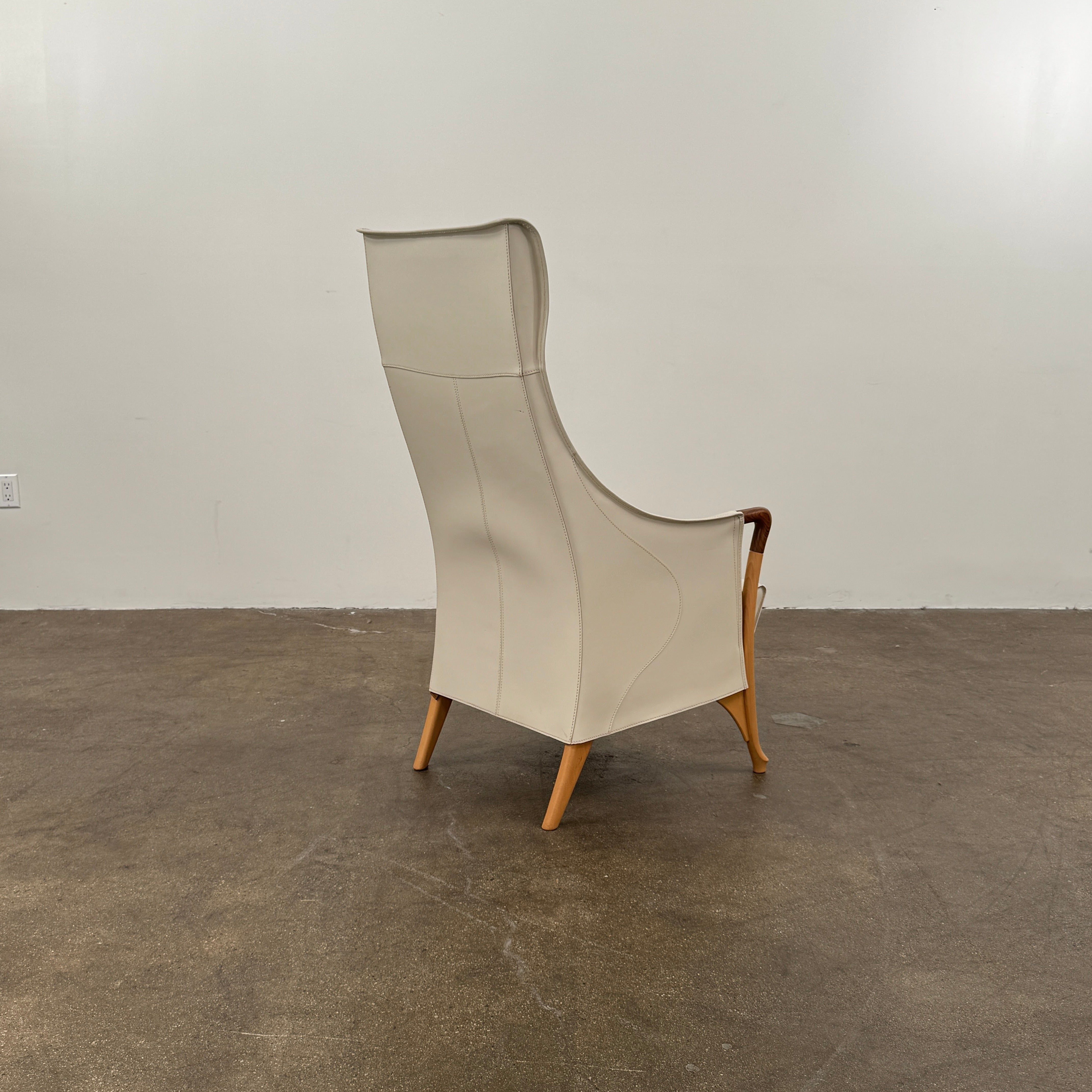 The Giorgetti “Progetti” Bergère / High-Back Lounge Chair by Giorgetti features light beige upholstery, wooden armrests and legs, and elegant ivory saddle leather accents, all inspired by the sophisticated Progetti collection, and is showcased against a plain white background.