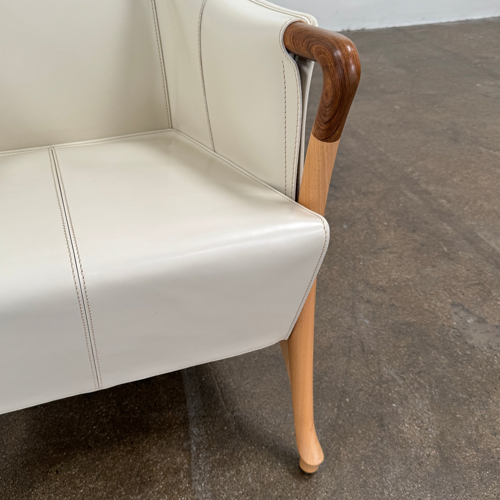 The Giorgetti “Progetti” Bergère / High-Back Lounge Chair by Giorgetti features light beige upholstery, wooden armrests and legs, and elegant ivory saddle leather accents, all inspired by the sophisticated Progetti collection, and is showcased against a plain white background.