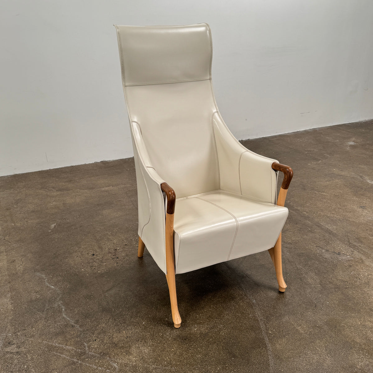 The Giorgetti “Progetti” Bergère / High-Back Lounge Chair by Giorgetti features light beige upholstery, wooden armrests and legs, and elegant ivory saddle leather accents, all inspired by the sophisticated Progetti collection, and is showcased against a plain white background.