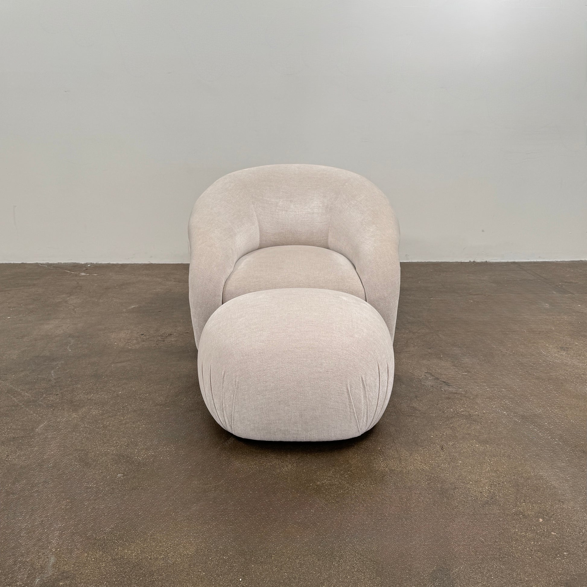 Certainly! Here’s a rewritten version of the sentence using your product data: The Vintage Chair + Ottoman – In The Style of Steve Chase by Vintage, featuring beige upholstery with rounded edges and a matching oval ottoman, both set against a plain white background, evoke the timeless elegance of mid-century modern furniture.
