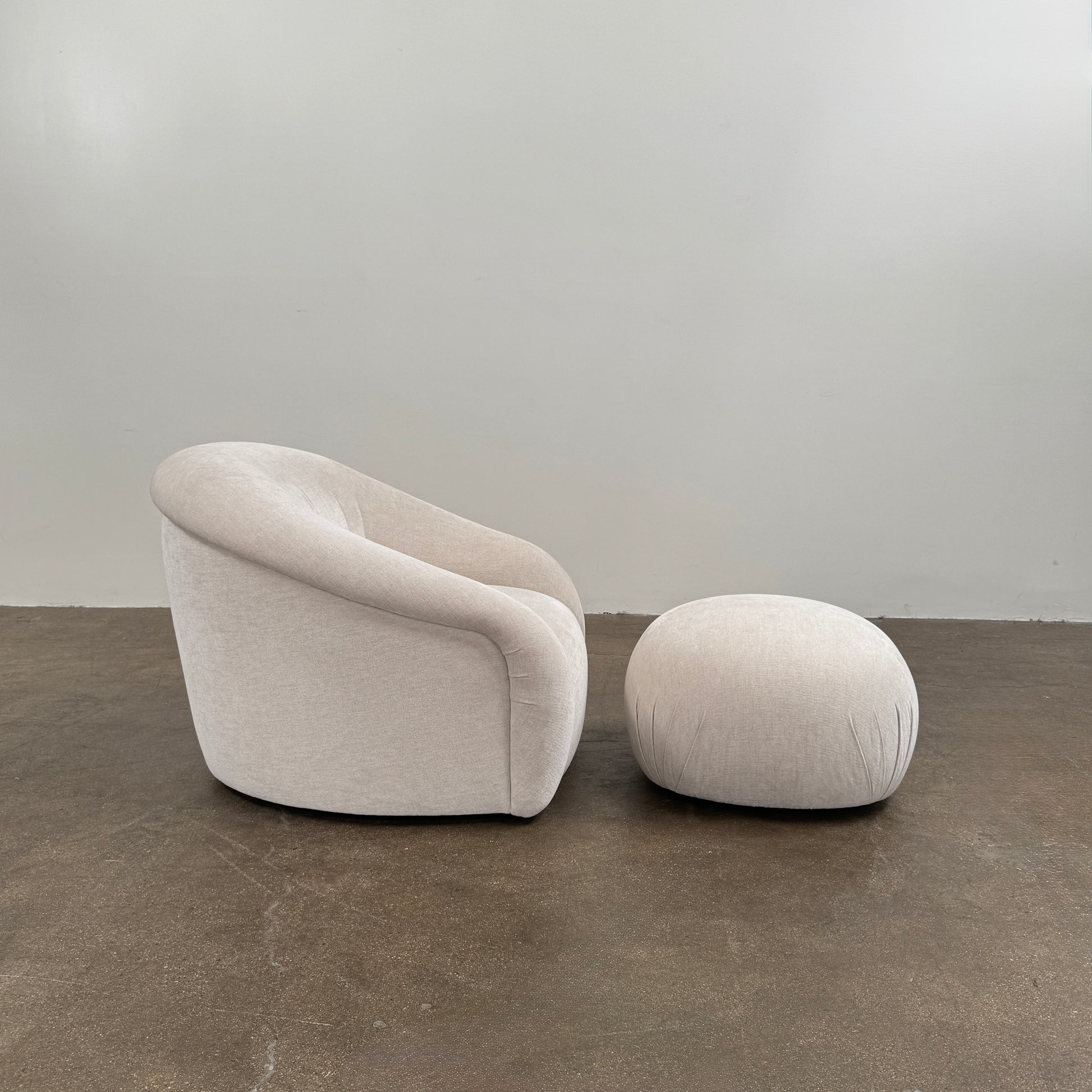 Certainly! Here’s a rewritten version of the sentence using your product data: The Vintage Chair + Ottoman – In The Style of Steve Chase by Vintage, featuring beige upholstery with rounded edges and a matching oval ottoman, both set against a plain white background, evoke the timeless elegance of mid-century modern furniture.