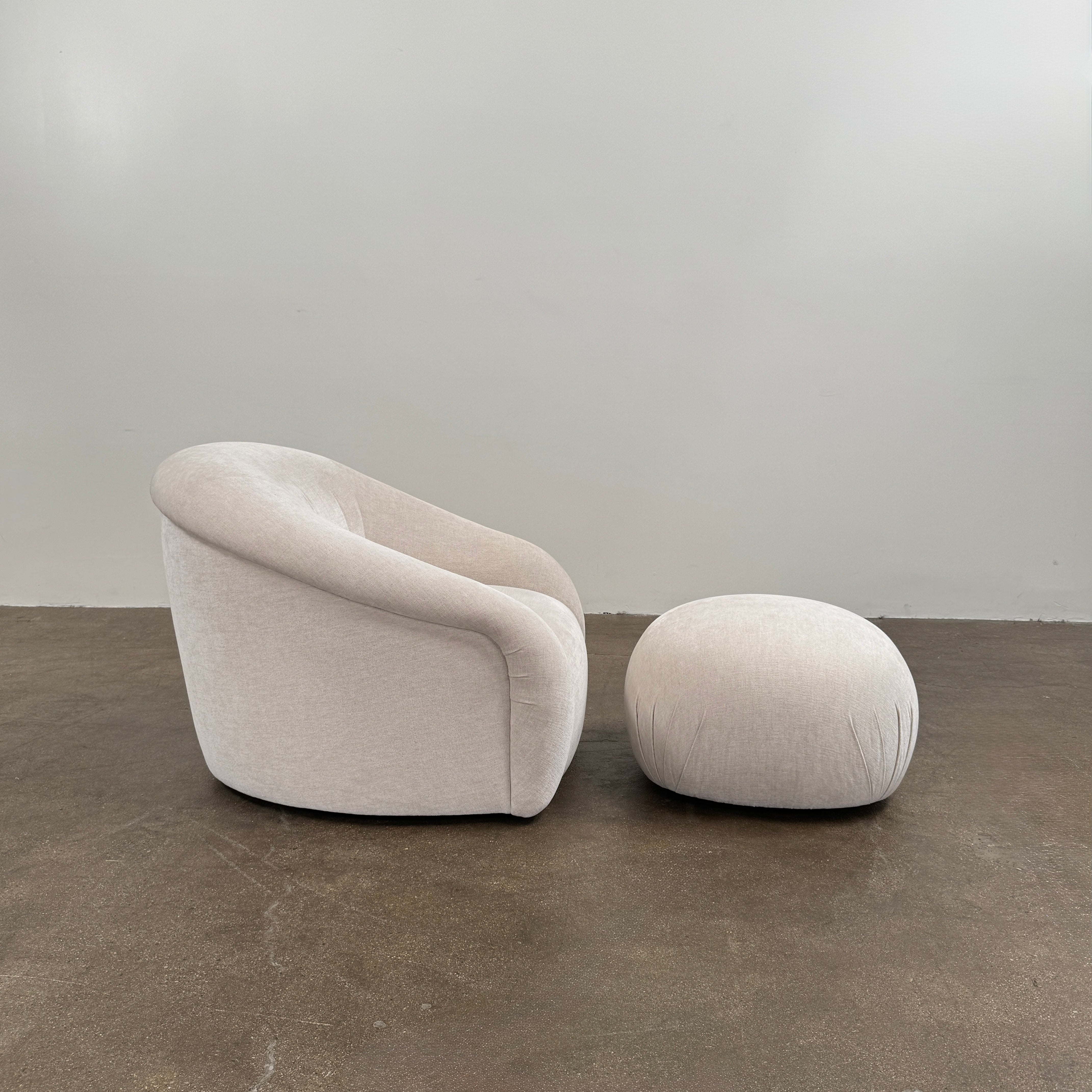 Certainly! Here’s a rewritten version of the sentence using your product data: The Vintage Chair + Ottoman – In The Style of Steve Chase by Vintage, featuring beige upholstery with rounded edges and a matching oval ottoman, both set against a plain white background, evoke the timeless elegance of mid-century modern furniture.
