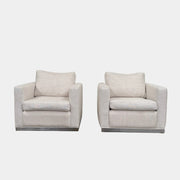 Two identical Milo Baughman-style armchairs from Vintage, in a light beige color with boxy shapes and cushions, are arranged side by side on a bare concrete floor against a plain light wall, forming an elegant “Milo Baughman - In the style of - Armchair Set of 2.”.