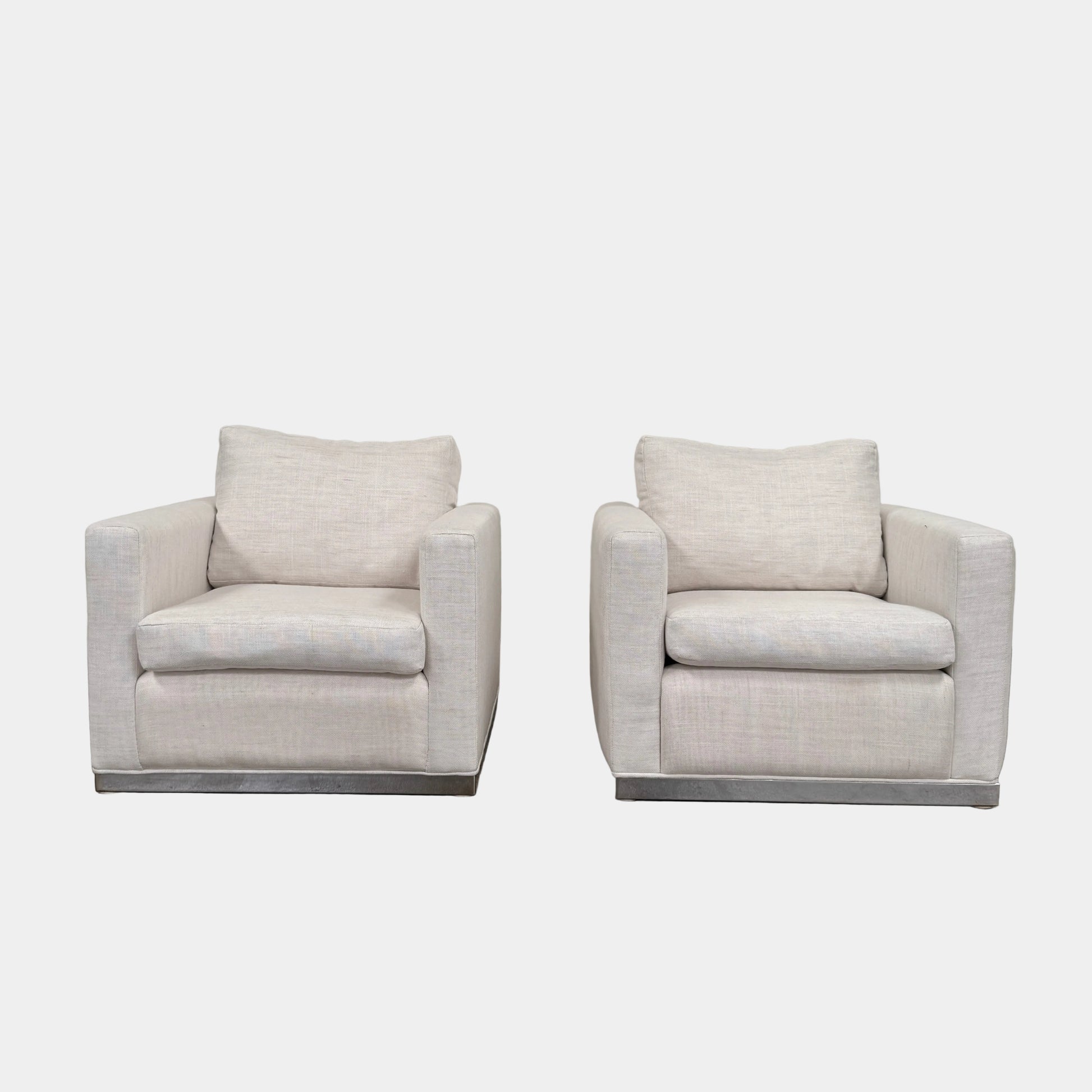 Two identical Milo Baughman-style armchairs from Vintage, in a light beige color with boxy shapes and cushions, are arranged side by side on a bare concrete floor against a plain light wall, forming an elegant “Milo Baughman - In the style of - Armchair Set of 2.”.