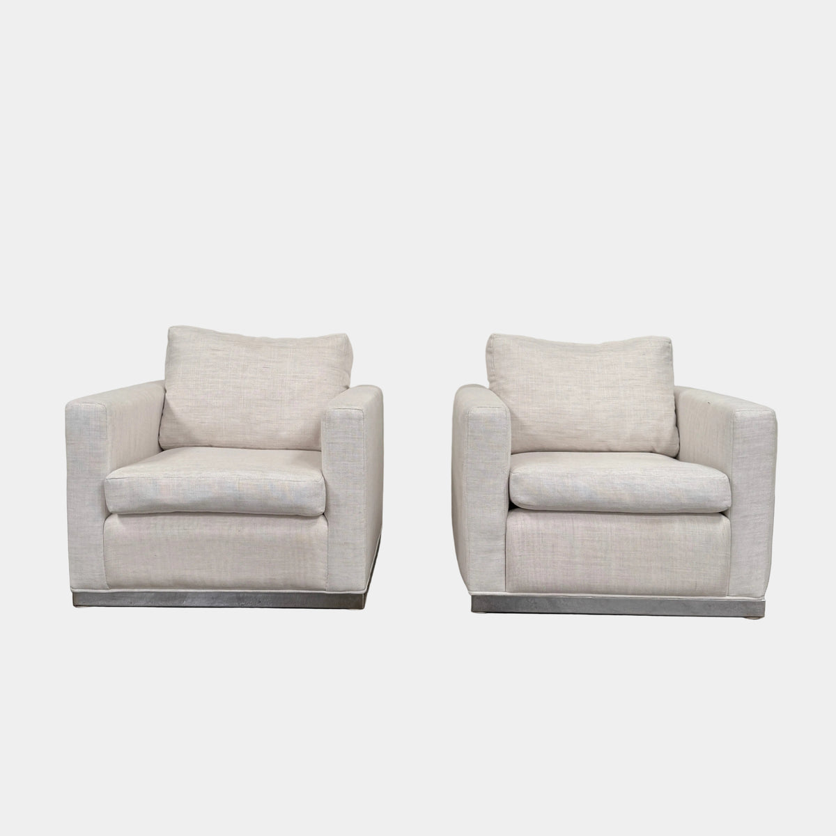 Two identical Milo Baughman-style armchairs from Vintage, in a light beige color with boxy shapes and cushions, are arranged side by side on a bare concrete floor against a plain light wall, forming an elegant “Milo Baughman - In the style of - Armchair Set of 2.”.