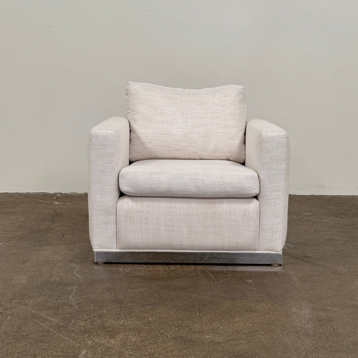 Two identical Milo Baughman-style armchairs from Vintage, in a light beige color with boxy shapes and cushions, are arranged side by side on a bare concrete floor against a plain light wall, forming an elegant “Milo Baughman - In the style of - Armchair Set of 2.”.