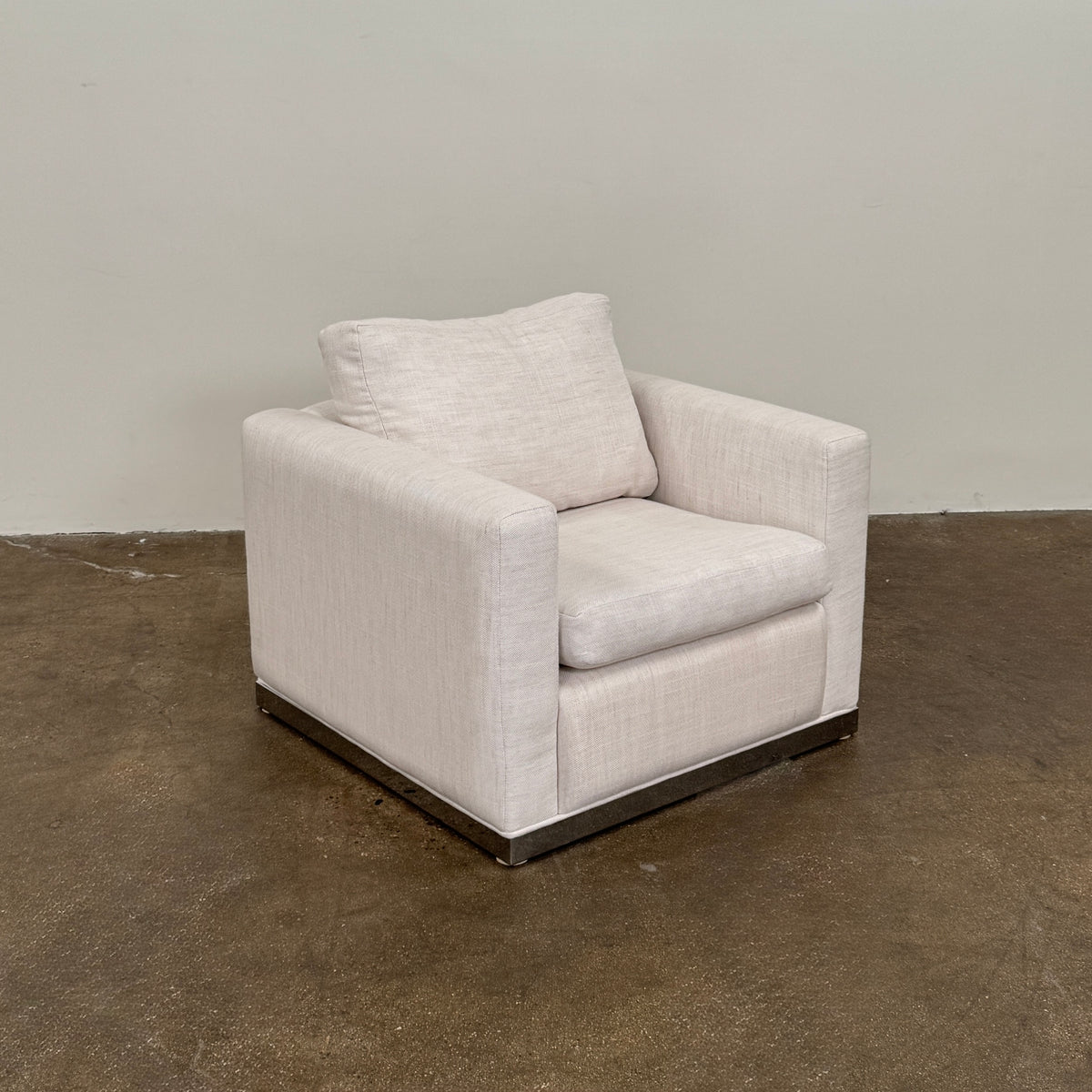 Two identical Milo Baughman-style armchairs from Vintage, in a light beige color with boxy shapes and cushions, are arranged side by side on a bare concrete floor against a plain light wall, forming an elegant “Milo Baughman - In the style of - Armchair Set of 2.”.