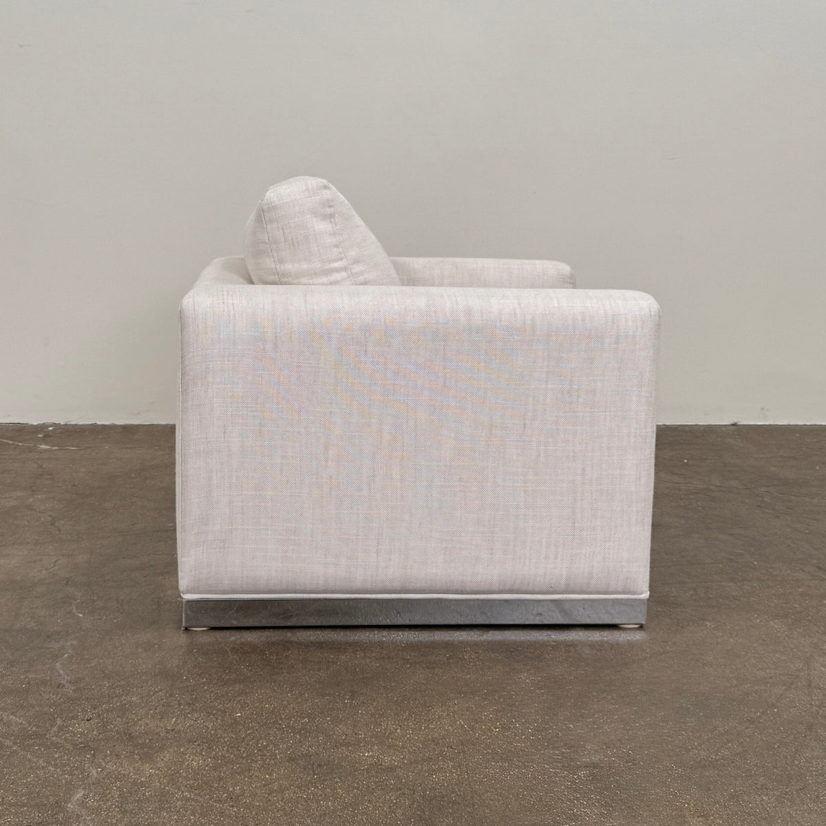 Two identical Milo Baughman-style armchairs from Vintage, in a light beige color with boxy shapes and cushions, are arranged side by side on a bare concrete floor against a plain light wall, forming an elegant “Milo Baughman - In the style of - Armchair Set of 2.”.