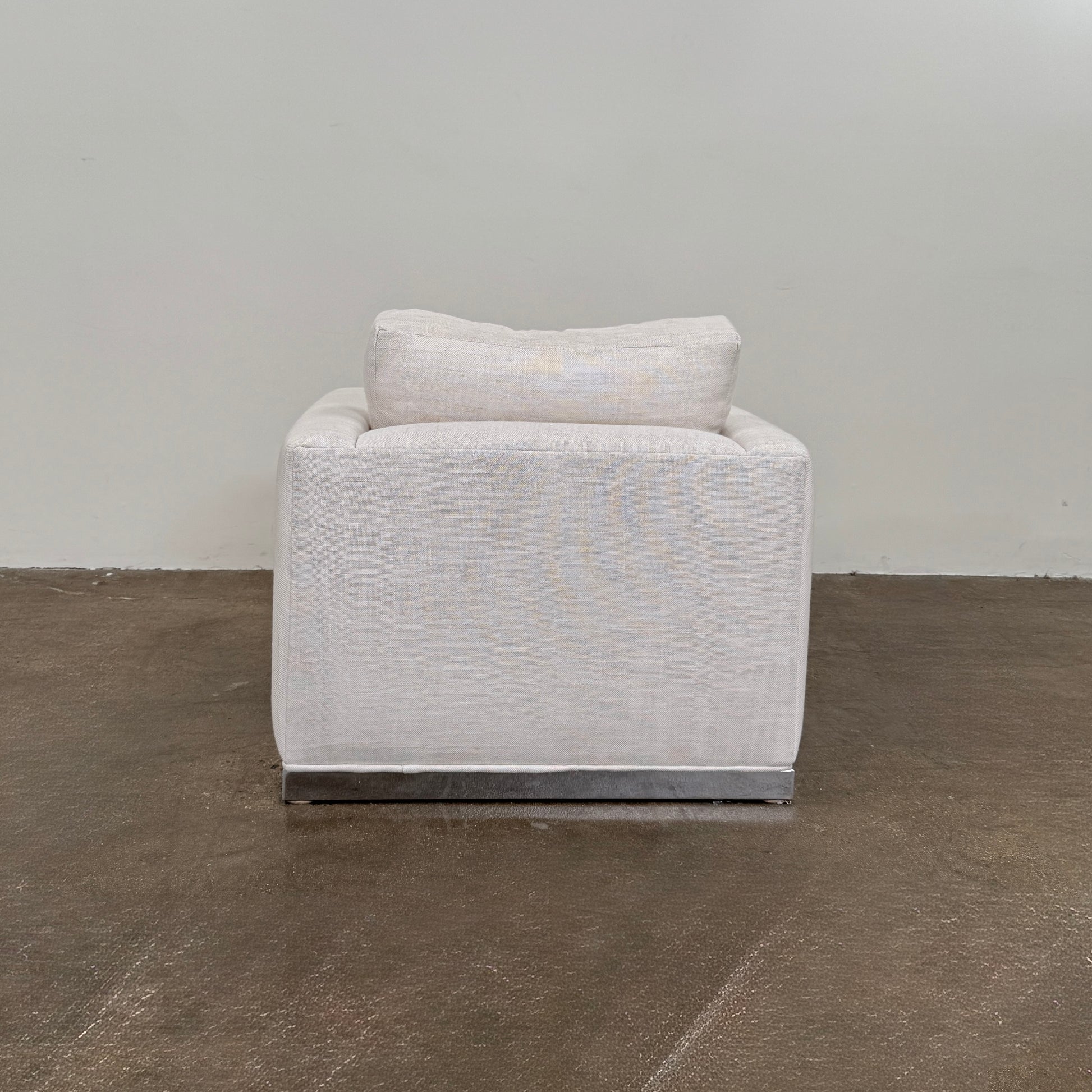 Two identical Milo Baughman-style armchairs from Vintage, in a light beige color with boxy shapes and cushions, are arranged side by side on a bare concrete floor against a plain light wall, forming an elegant “Milo Baughman - In the style of - Armchair Set of 2.”.
