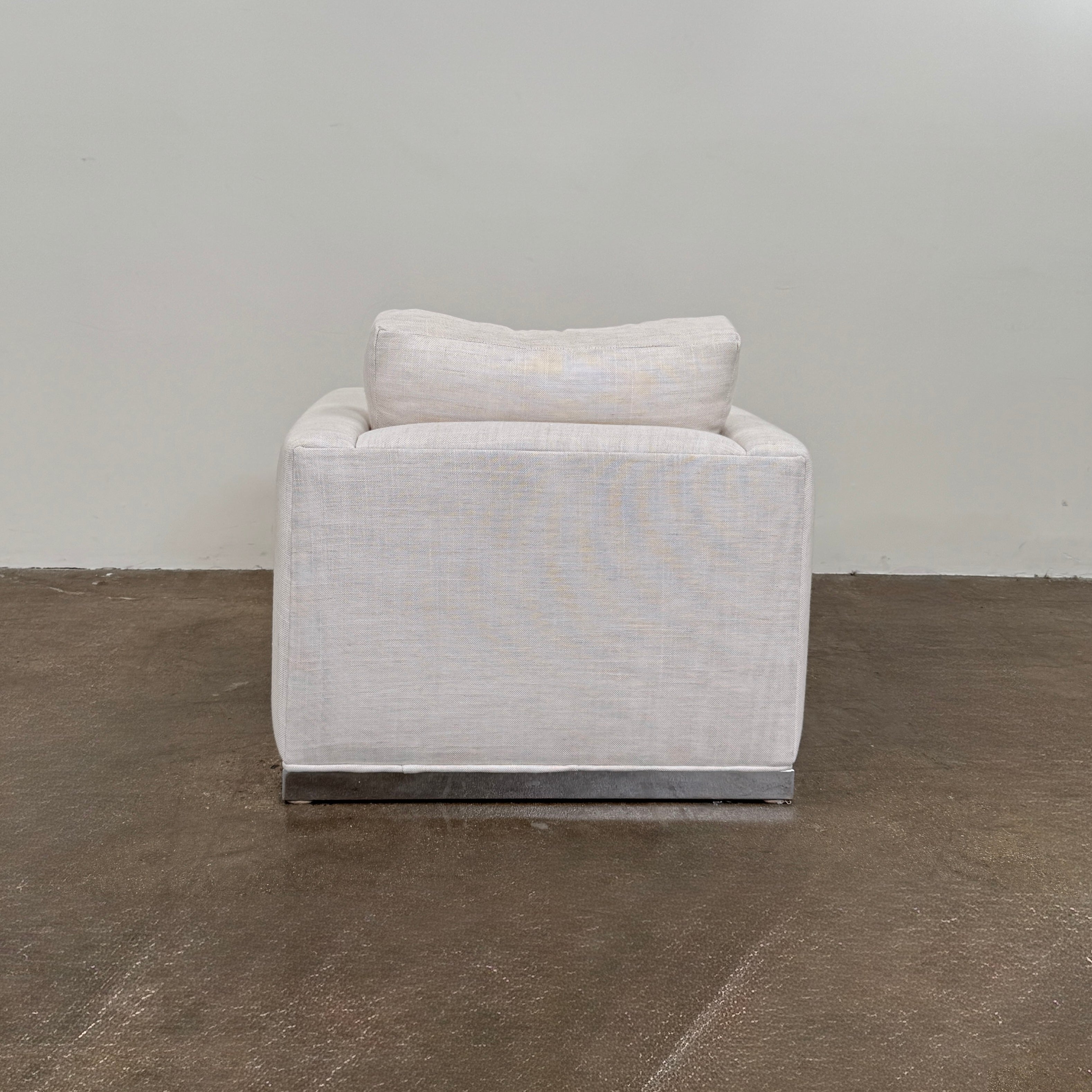 Two identical Milo Baughman-style armchairs from Vintage, in a light beige color with boxy shapes and cushions, are arranged side by side on a bare concrete floor against a plain light wall, forming an elegant “Milo Baughman - In the style of - Armchair Set of 2.”.