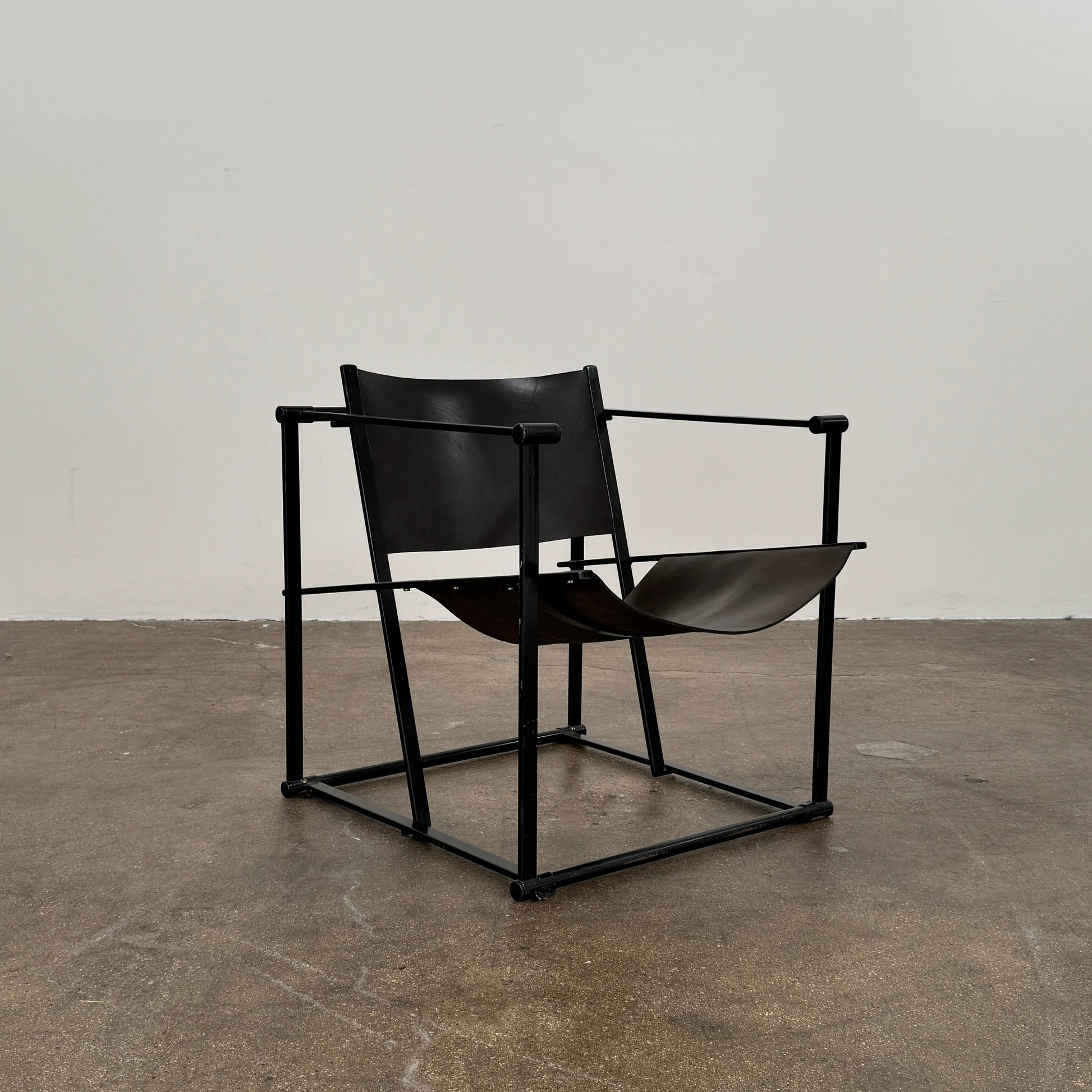 Two Pastoe FM62 chairs in black leather by Modern Resale are positioned side by side on a brown concrete floor against a plain white wall.