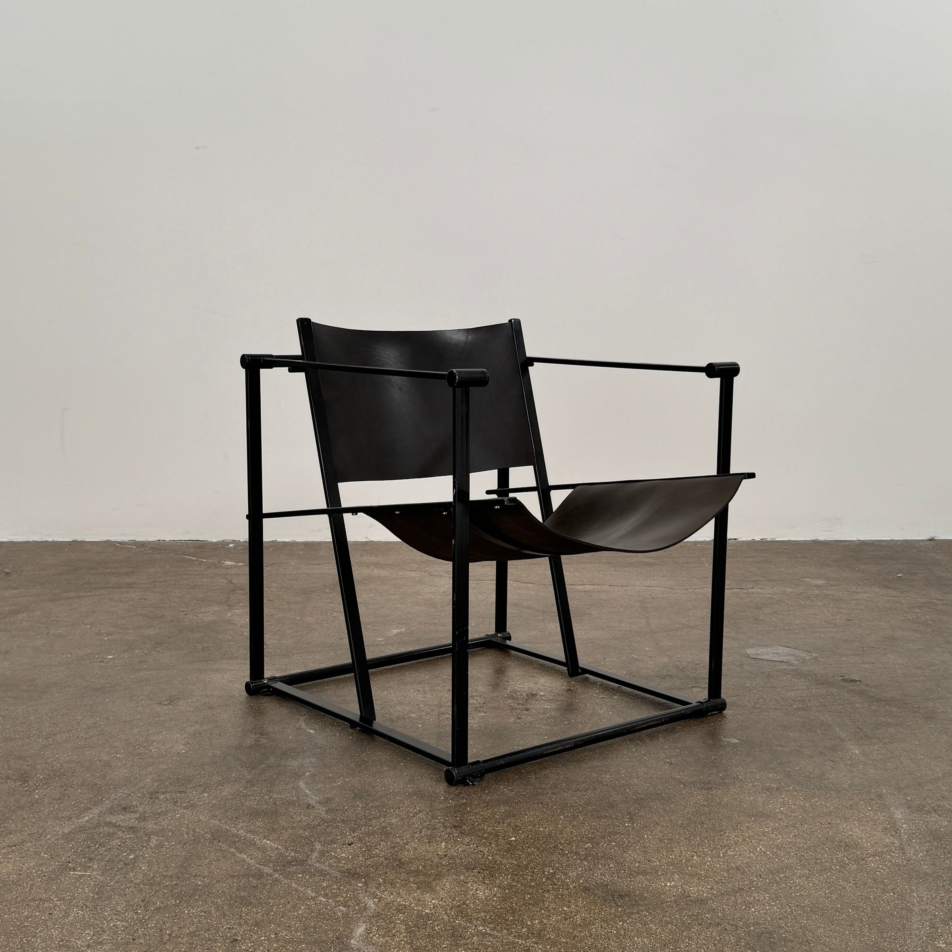 Two Pastoe FM62 chairs in black leather by Modern Resale are positioned side by side on a brown concrete floor against a plain white wall.