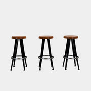 A set of three Vintage Stools in the style of Jean Prouve by Vintage, featuring black metal frames, round brown wooden seats, and silver footrests, are arranged in a row against a plain white background, evoking a classic mid-century design.