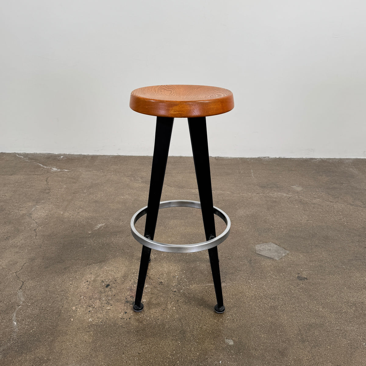 A set of three Vintage Stools in the style of Jean Prouve by Vintage, featuring black metal frames, round brown wooden seats, and silver footrests, are arranged in a row against a plain white background, evoking a classic mid-century design.