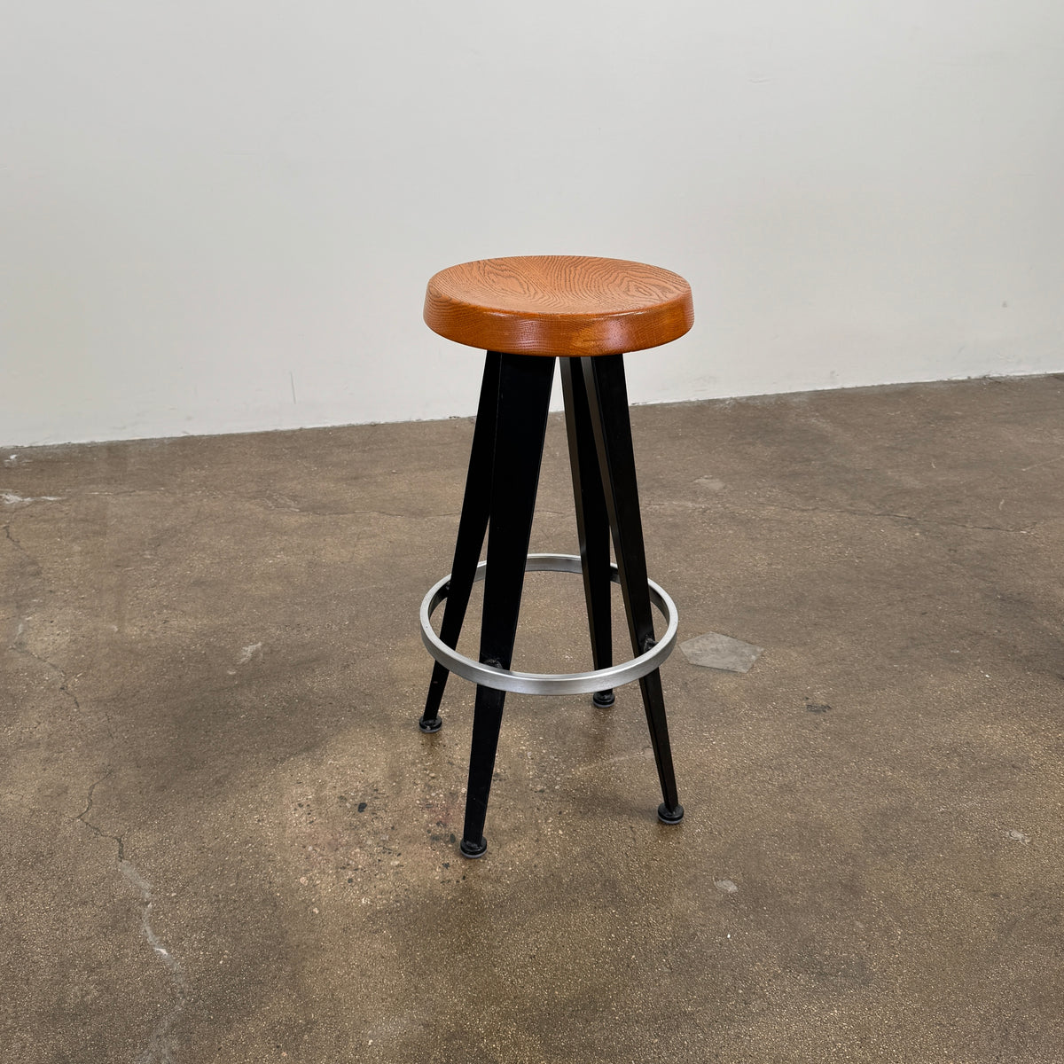 A set of three Vintage Stools in the style of Jean Prouve by Vintage, featuring black metal frames, round brown wooden seats, and silver footrests, are arranged in a row against a plain white background, evoking a classic mid-century design.