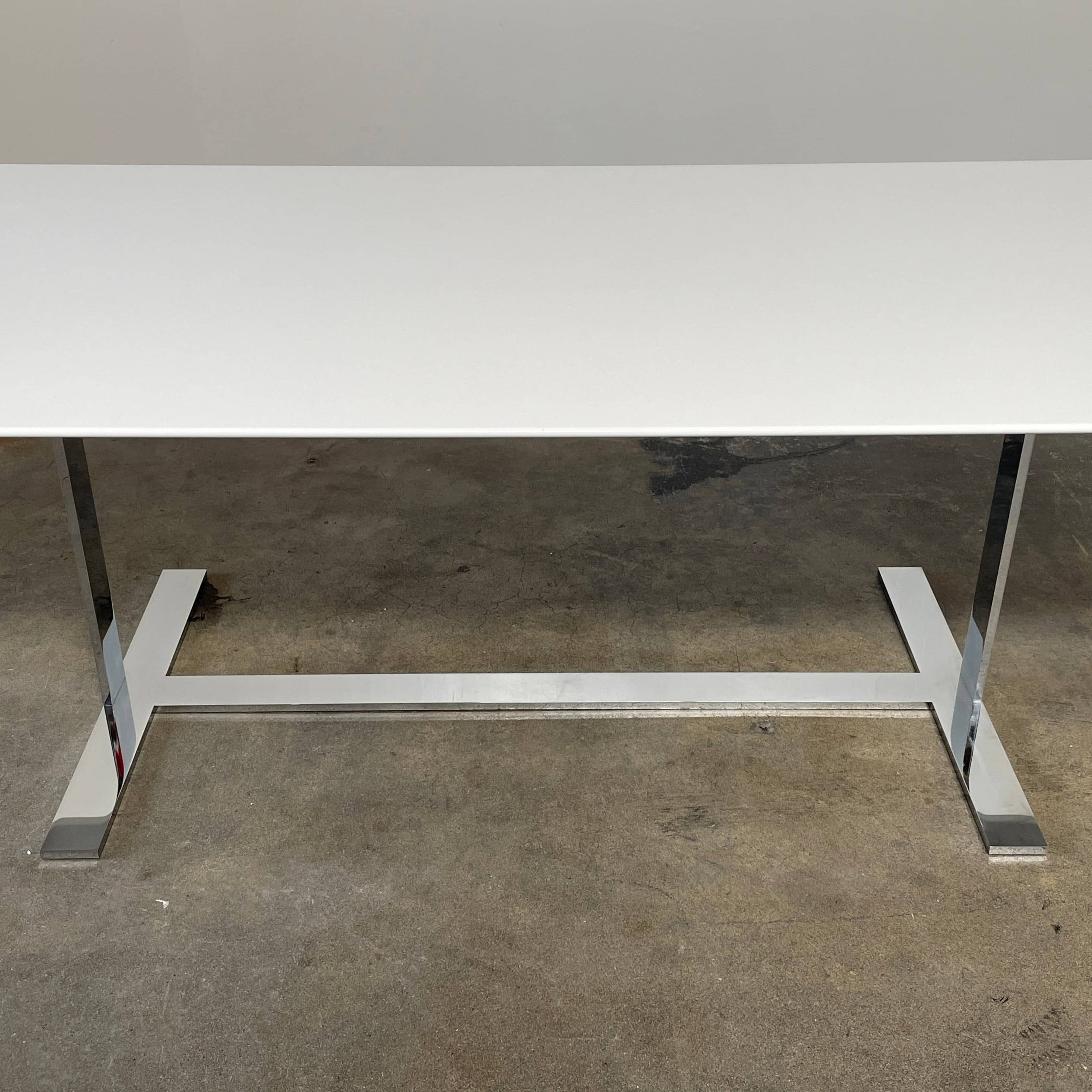 A minimalist rectangular B&B Italia Eileen White Dining Table featuring a sophisticated T-shaped metal base on a plain white background.