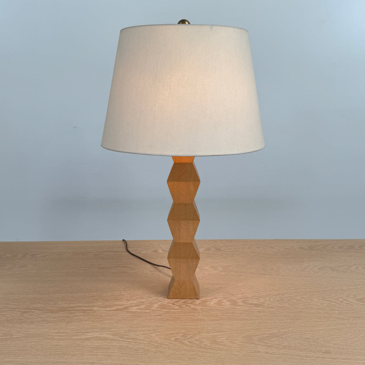 The Donghia Zig Zag Lamp Pickled Oak by Donghia features a white fabric shade and geometric wooden base, displayed on a light wood surface against a plain background.