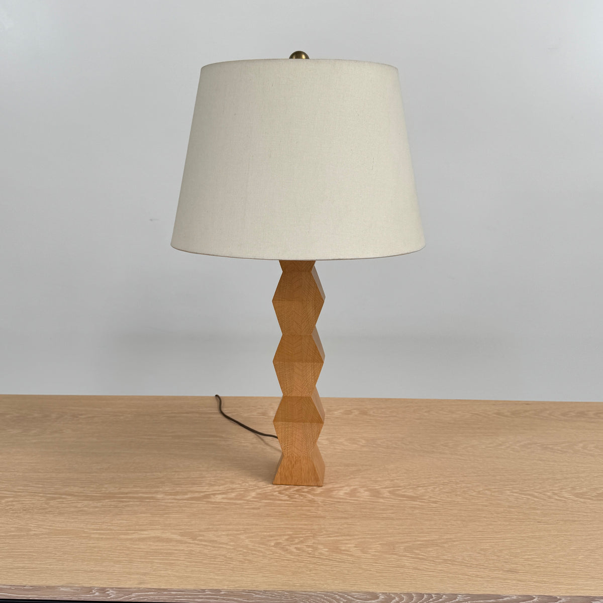 The Donghia Zig Zag Lamp Pickled Oak by Donghia features a white fabric shade and geometric wooden base, displayed on a light wood surface against a plain background.