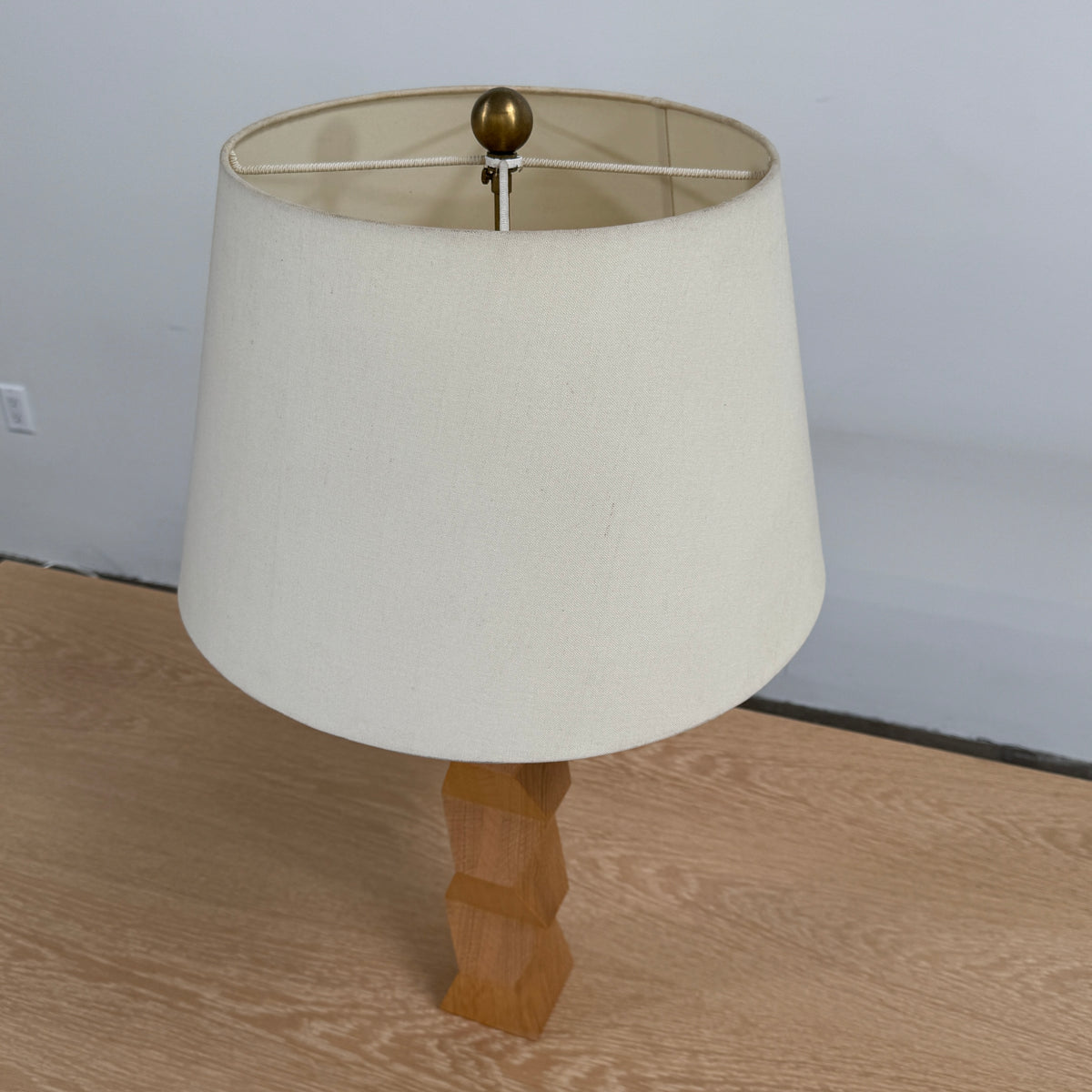 The Donghia Zig Zag Lamp Pickled Oak by Donghia features a white fabric shade and geometric wooden base, displayed on a light wood surface against a plain background.