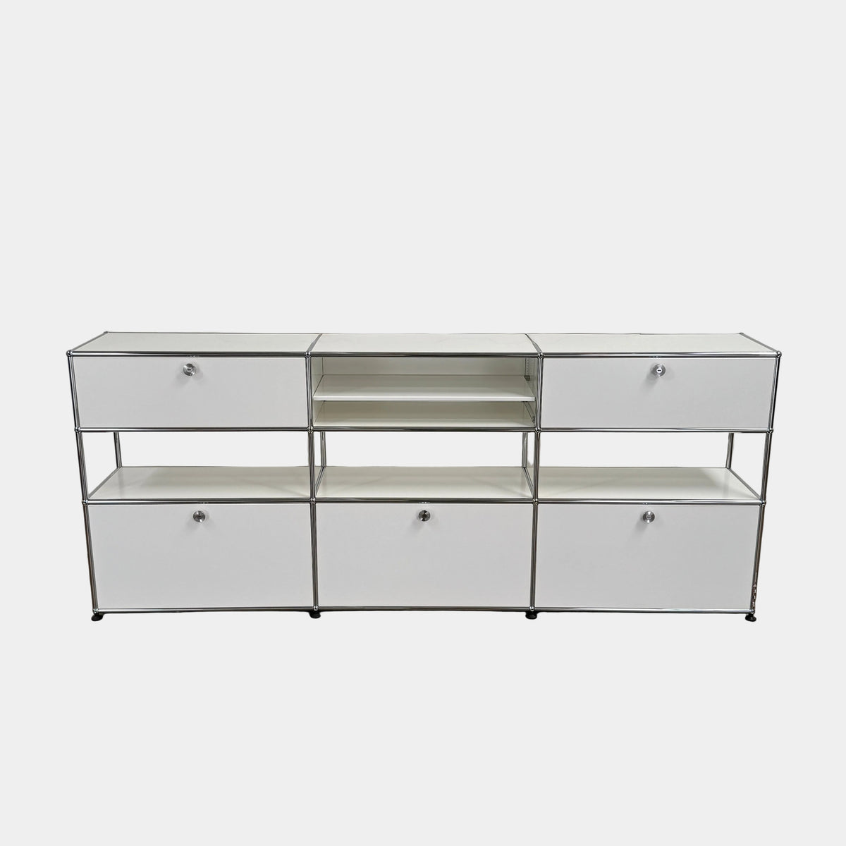 A USM Haller Storage Cabinet by USM, finished in minimal white, stands on a plain concrete floor against a light-colored wall. The modular cabinet features six closed compartments, two open shelves, and a sturdy metal frame.