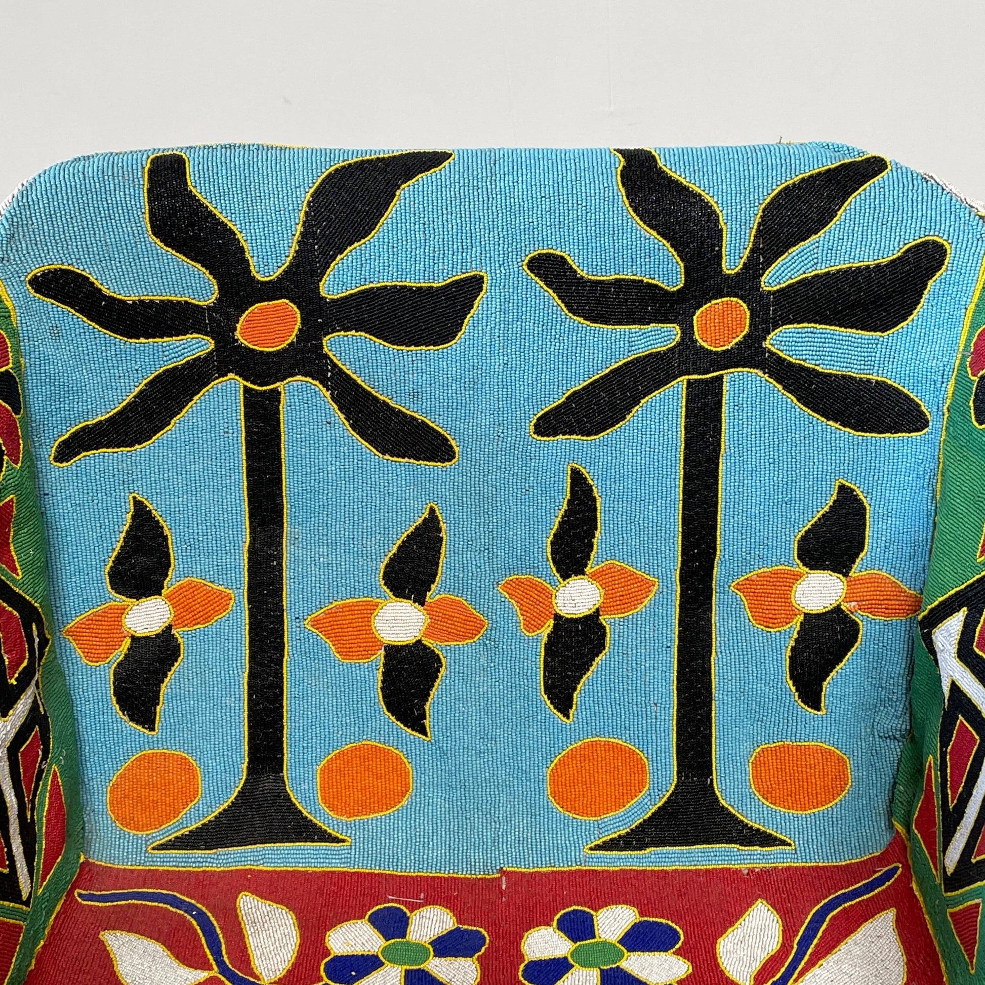 The Handmade Hand Beaded African Yoruba Chair (on hold) features a high backrest, wooden legs, and vibrant upholstery with multicolored geometric and floral patterns inspired by West African artistry.