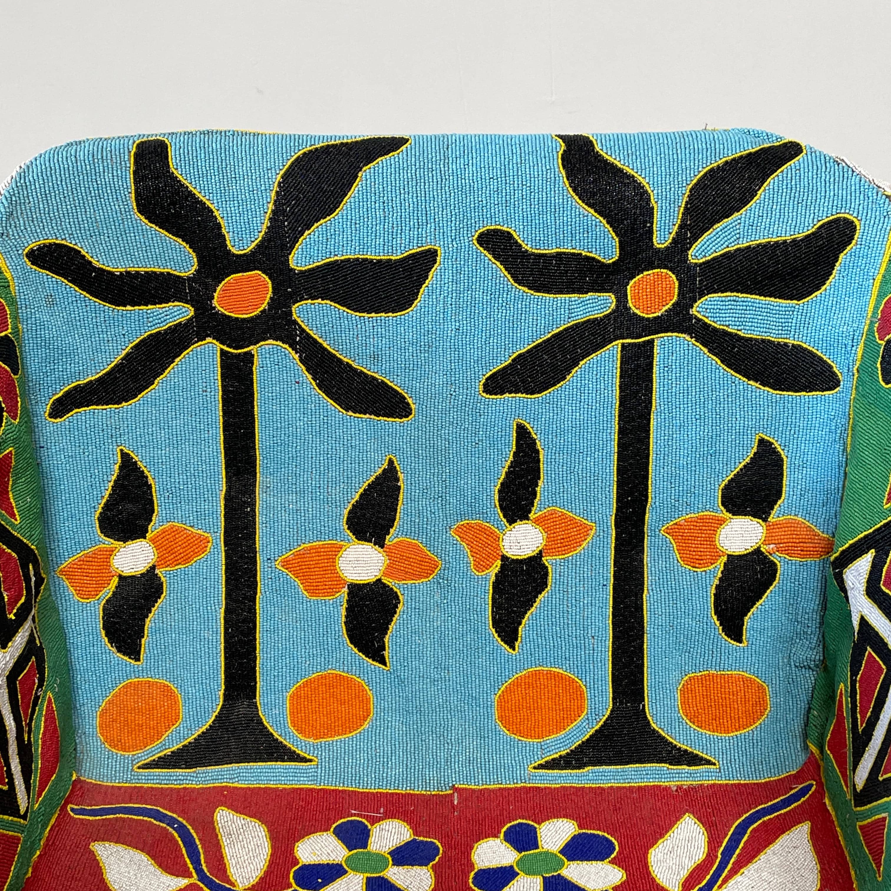 The Handmade Hand Beaded African Yoruba Chair (on hold) features a high backrest, wooden legs, and vibrant upholstery with multicolored geometric and floral patterns inspired by West African artistry.