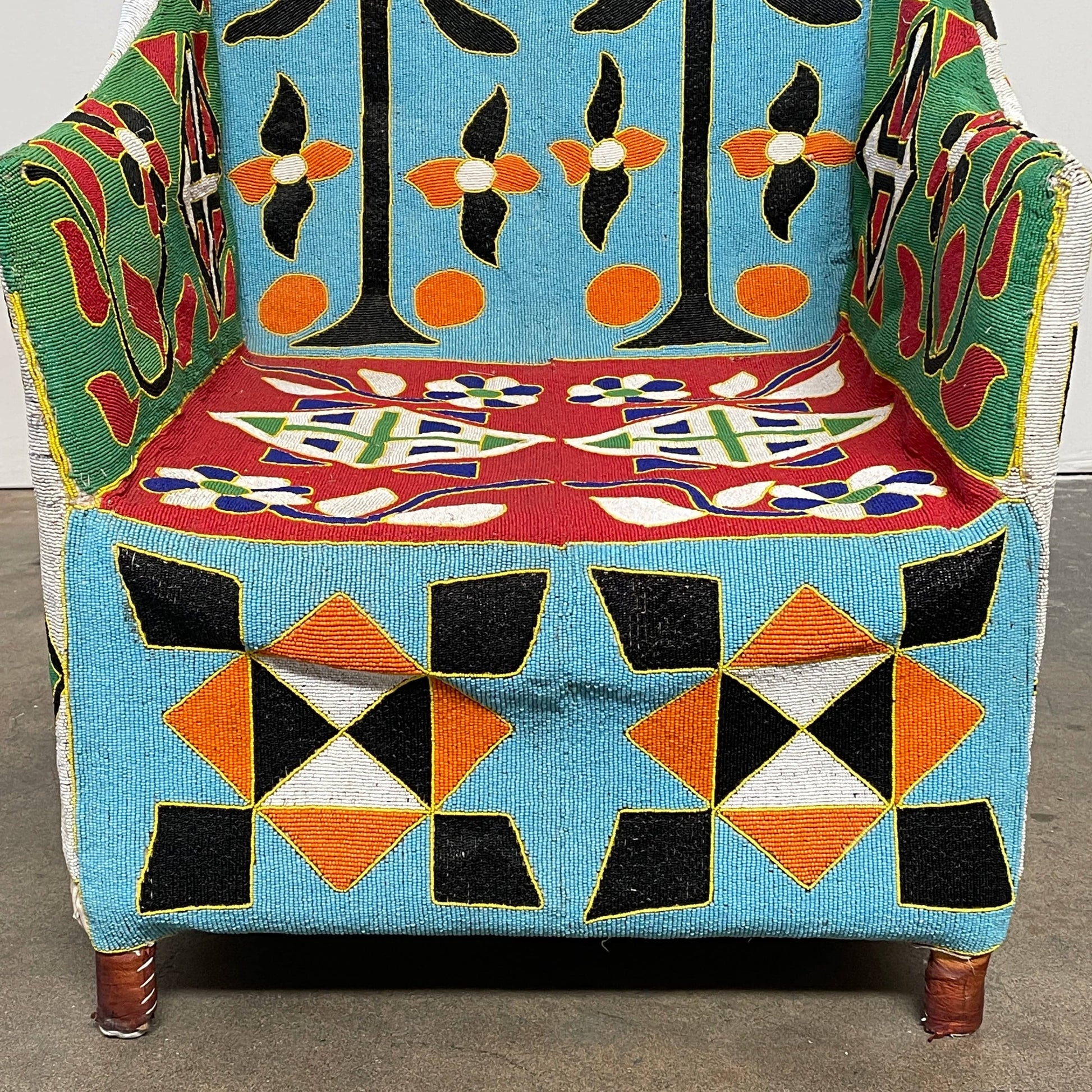 The Handmade Hand Beaded African Yoruba Chair (on hold) features a high backrest, wooden legs, and vibrant upholstery with multicolored geometric and floral patterns inspired by West African artistry.