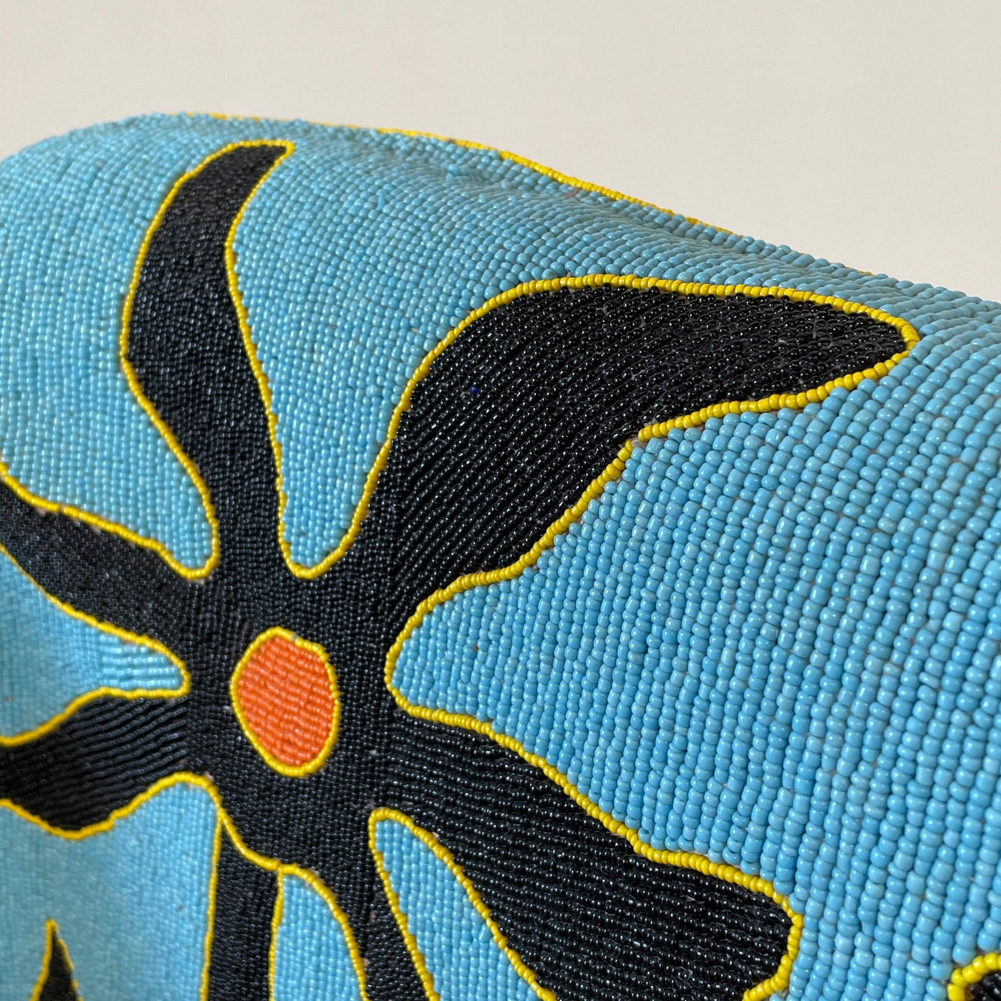 The Handmade Hand Beaded African Yoruba Chair (on hold) features a high backrest, wooden legs, and vibrant upholstery with multicolored geometric and floral patterns inspired by West African artistry.