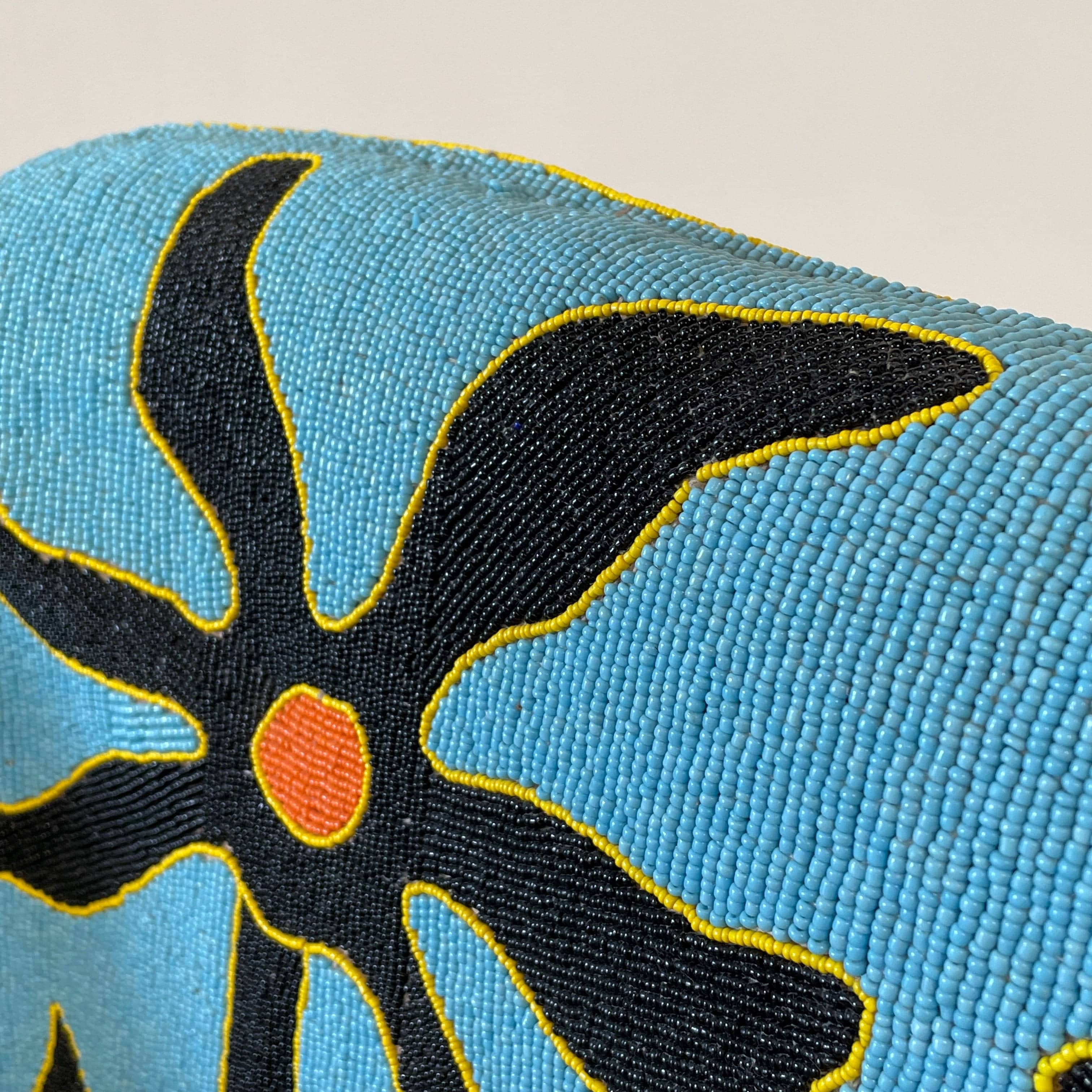 The Handmade Hand Beaded African Yoruba Chair (on hold) features a high backrest, wooden legs, and vibrant upholstery with multicolored geometric and floral patterns inspired by West African artistry.