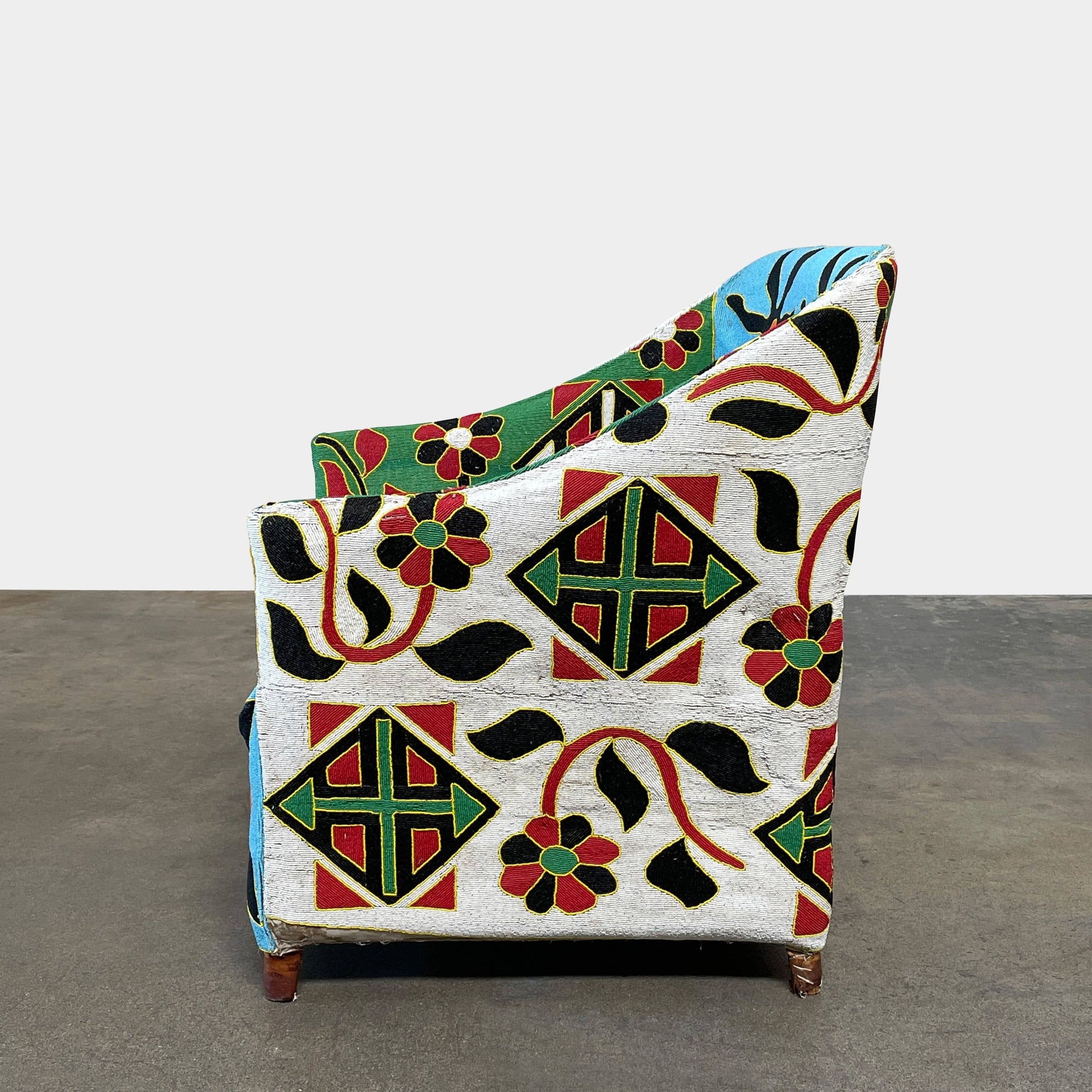 The Handmade Hand Beaded African Yoruba Chair (on hold) features a high backrest, wooden legs, and vibrant upholstery with multicolored geometric and floral patterns inspired by West African artistry.