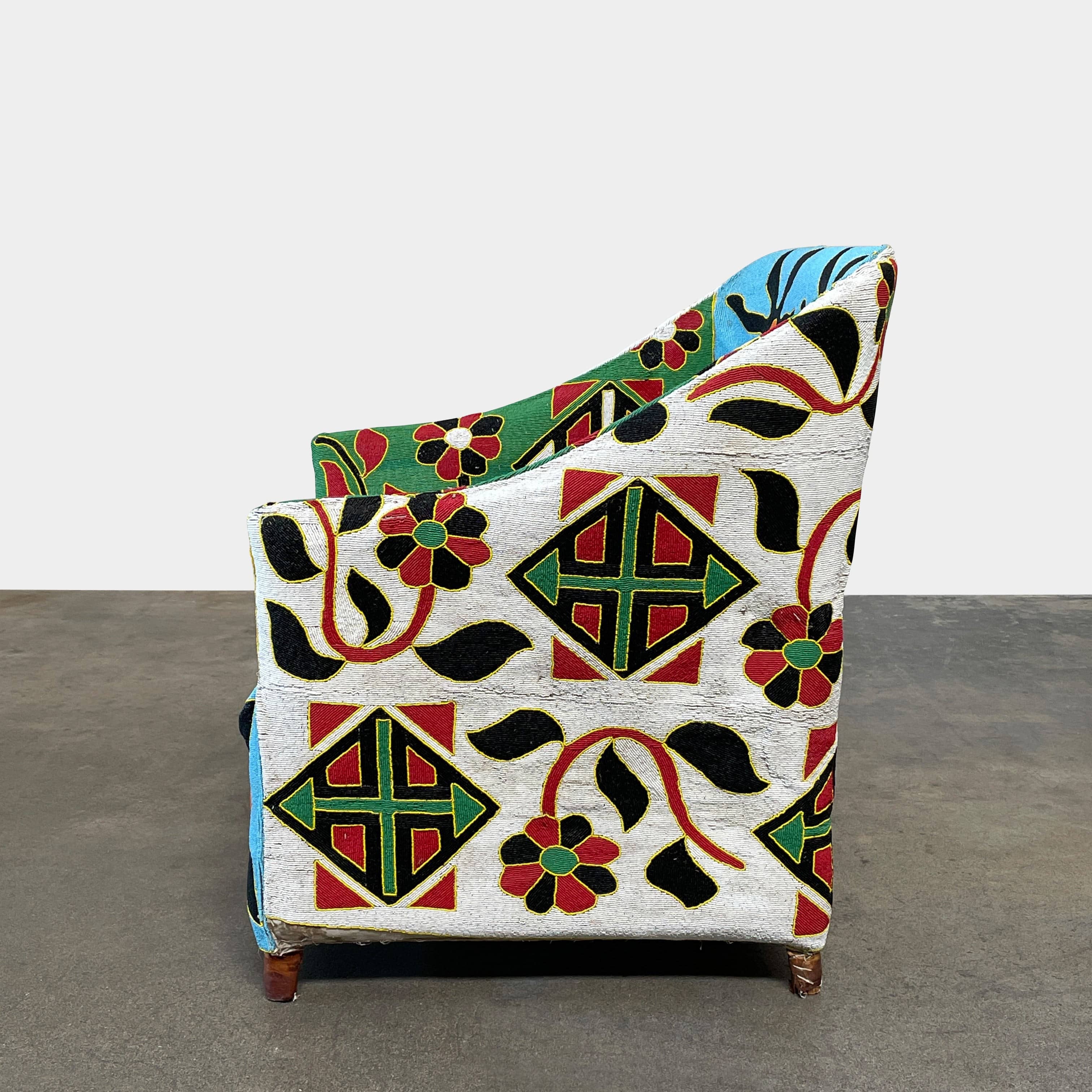 The Handmade Hand Beaded African Yoruba Chair (on hold) features a high backrest, wooden legs, and vibrant upholstery with multicolored geometric and floral patterns inspired by West African artistry.