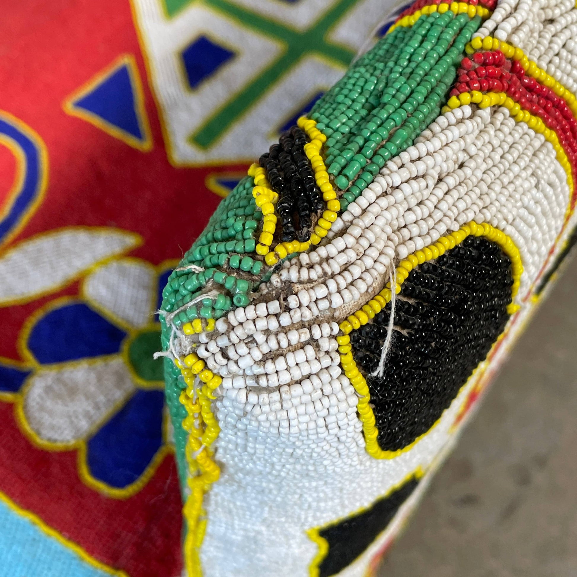 The Handmade Hand Beaded African Yoruba Chair (on hold) features a high backrest, wooden legs, and vibrant upholstery with multicolored geometric and floral patterns inspired by West African artistry.