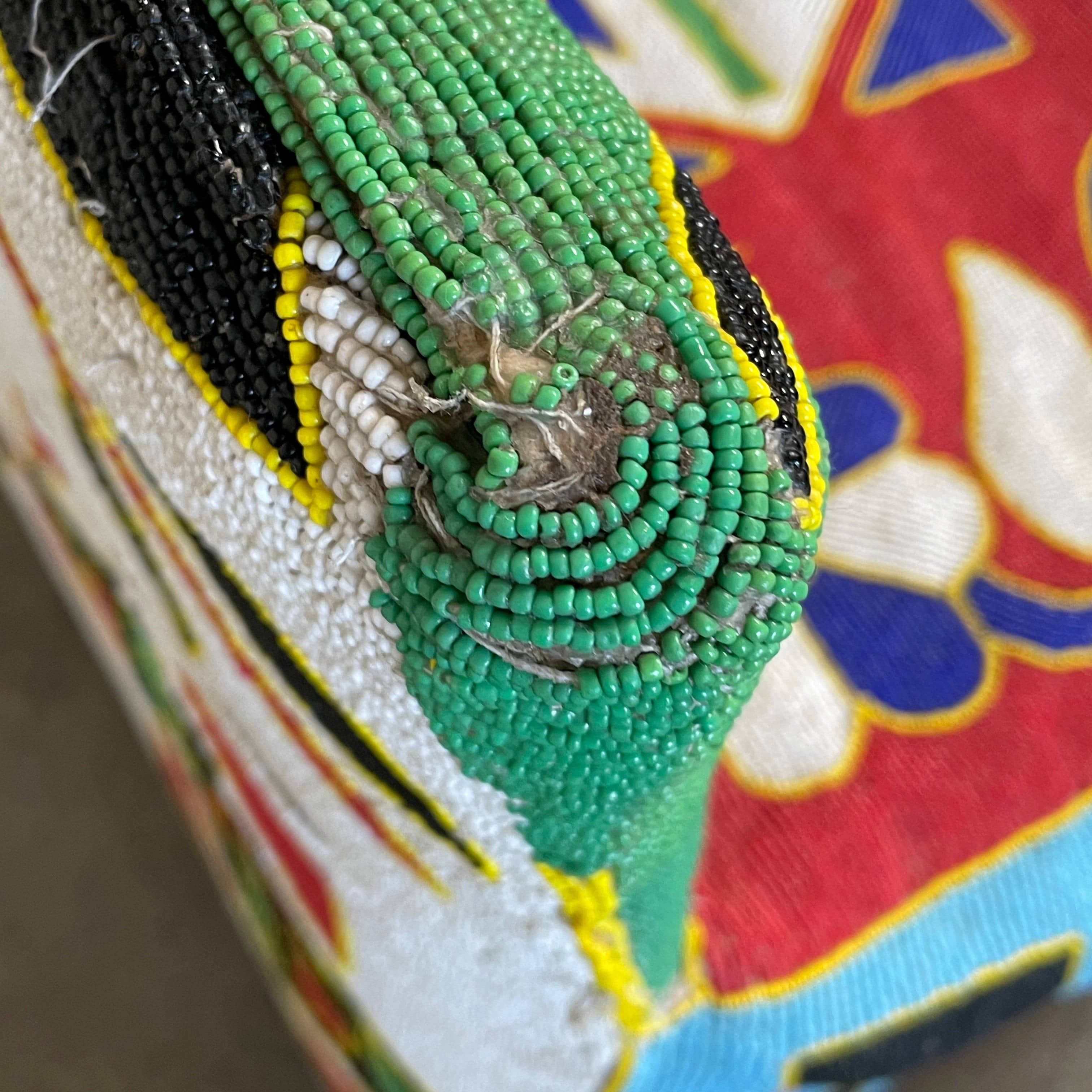 The Handmade Hand Beaded African Yoruba Chair (on hold) features a high backrest, wooden legs, and vibrant upholstery with multicolored geometric and floral patterns inspired by West African artistry.