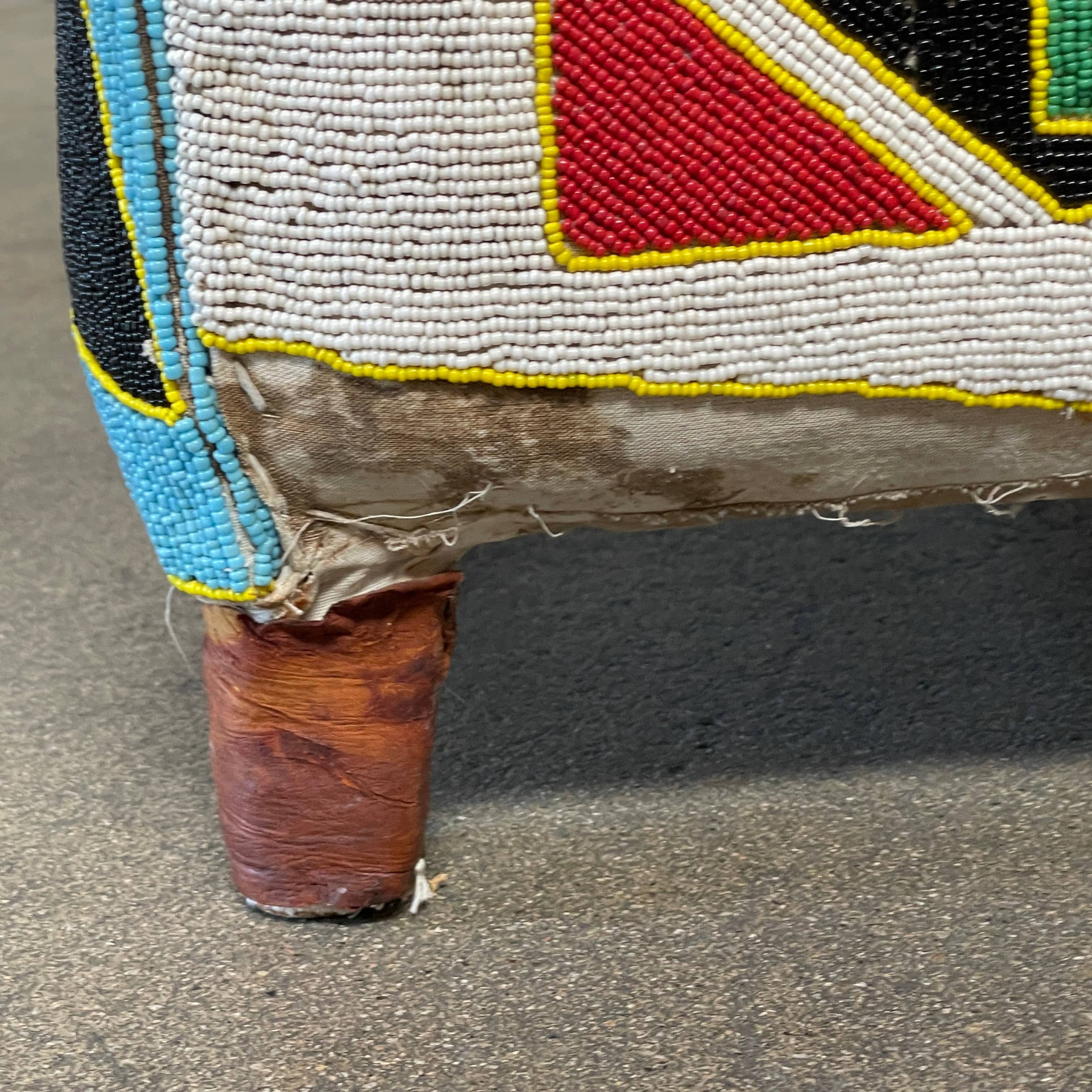 The Handmade Hand Beaded African Yoruba Chair (on hold) features a high backrest, wooden legs, and vibrant upholstery with multicolored geometric and floral patterns inspired by West African artistry.