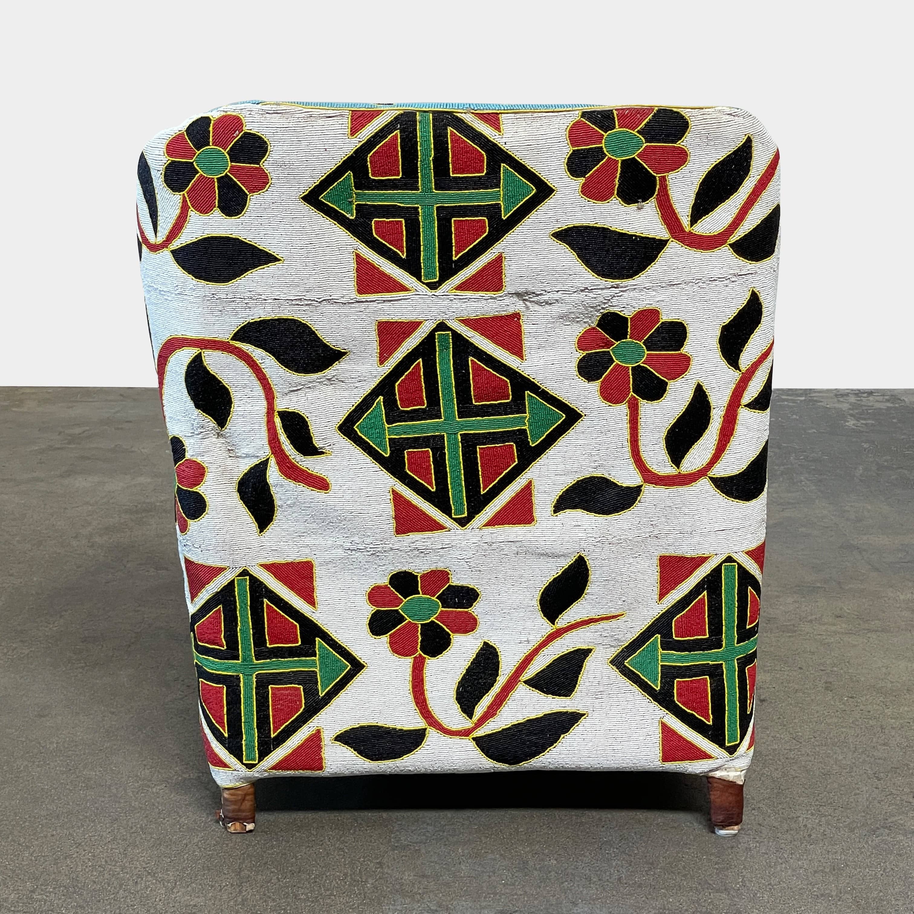 The Handmade Hand Beaded African Yoruba Chair (on hold) features a high backrest, wooden legs, and vibrant upholstery with multicolored geometric and floral patterns inspired by West African artistry.