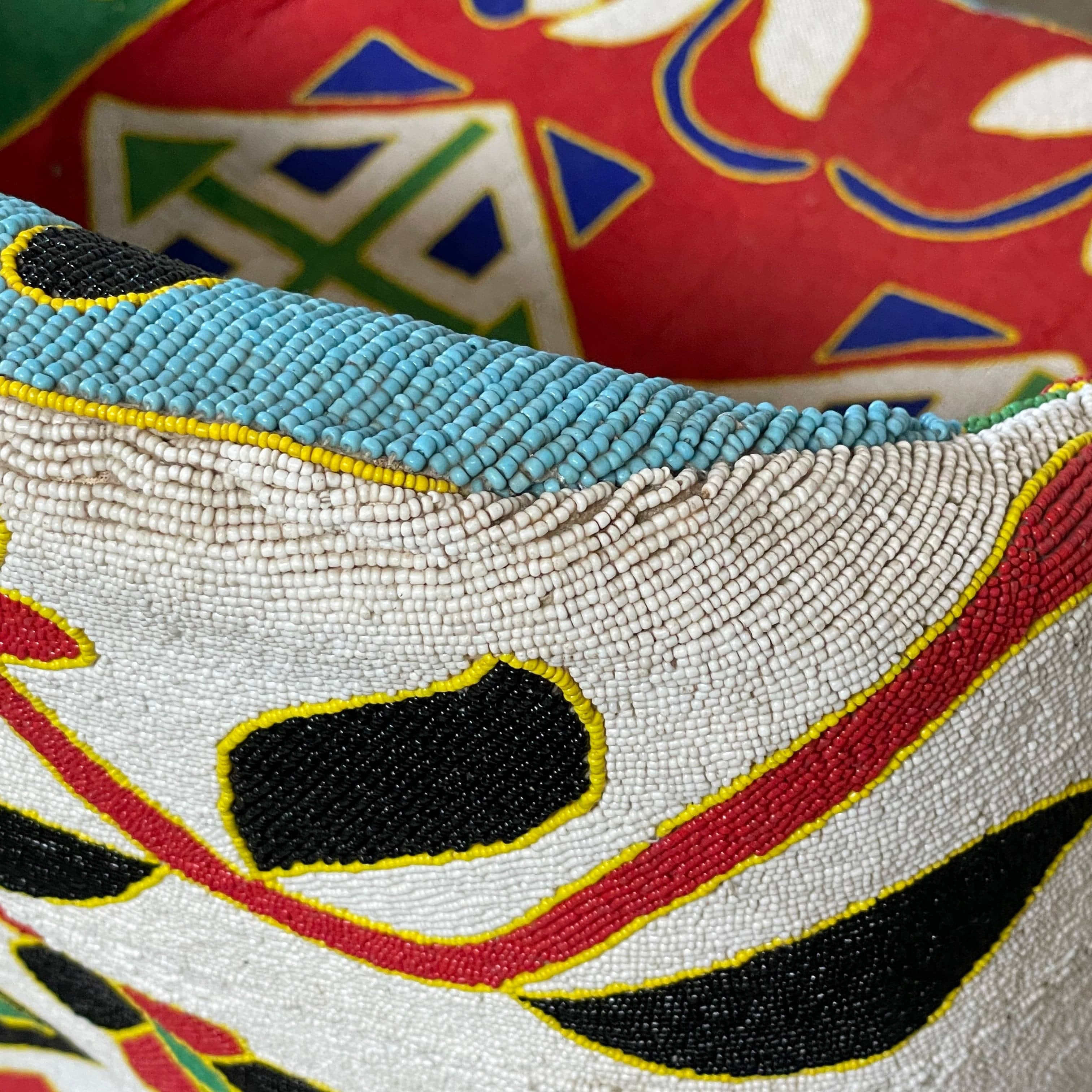 The Handmade Hand Beaded African Yoruba Chair (on hold) features a high backrest, wooden legs, and vibrant upholstery with multicolored geometric and floral patterns inspired by West African artistry.